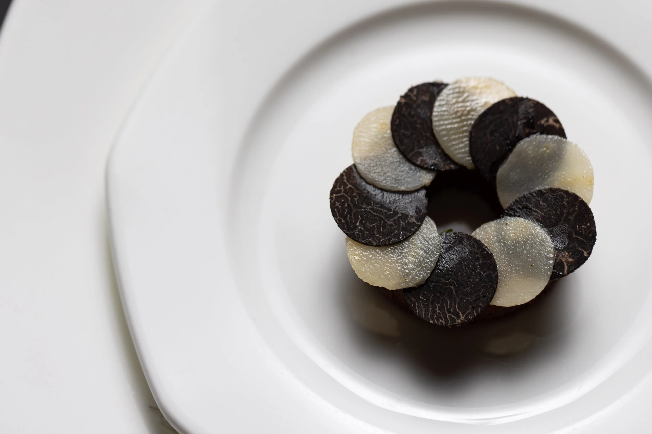 A ring-shaped dessert topped with alternating dark and white chocolate discs on a white plate