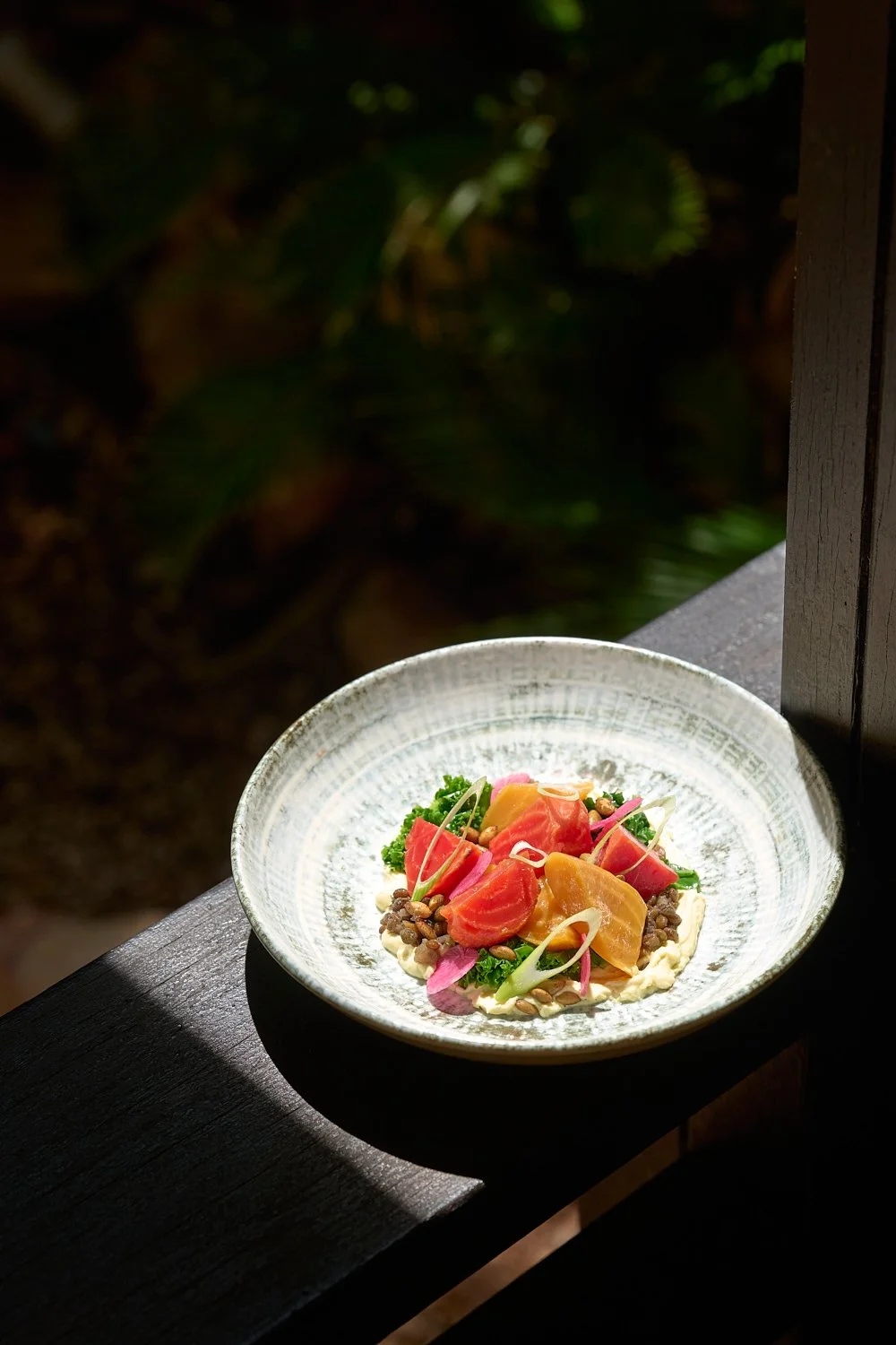 A plate with colorful sliced vegetables, possibly including tomatoes, pickles, onions, and greens, presented on a light-colored dish with a dark background.