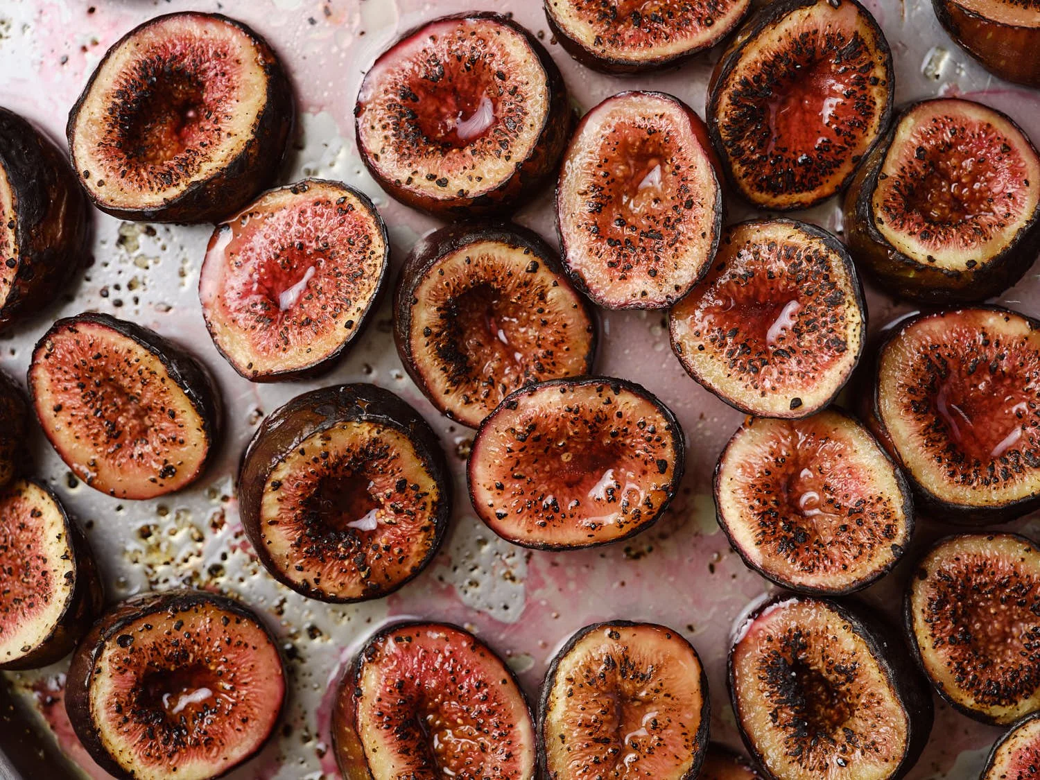 Halved ripe figs with black seeds on a white surface with some liquid droplets