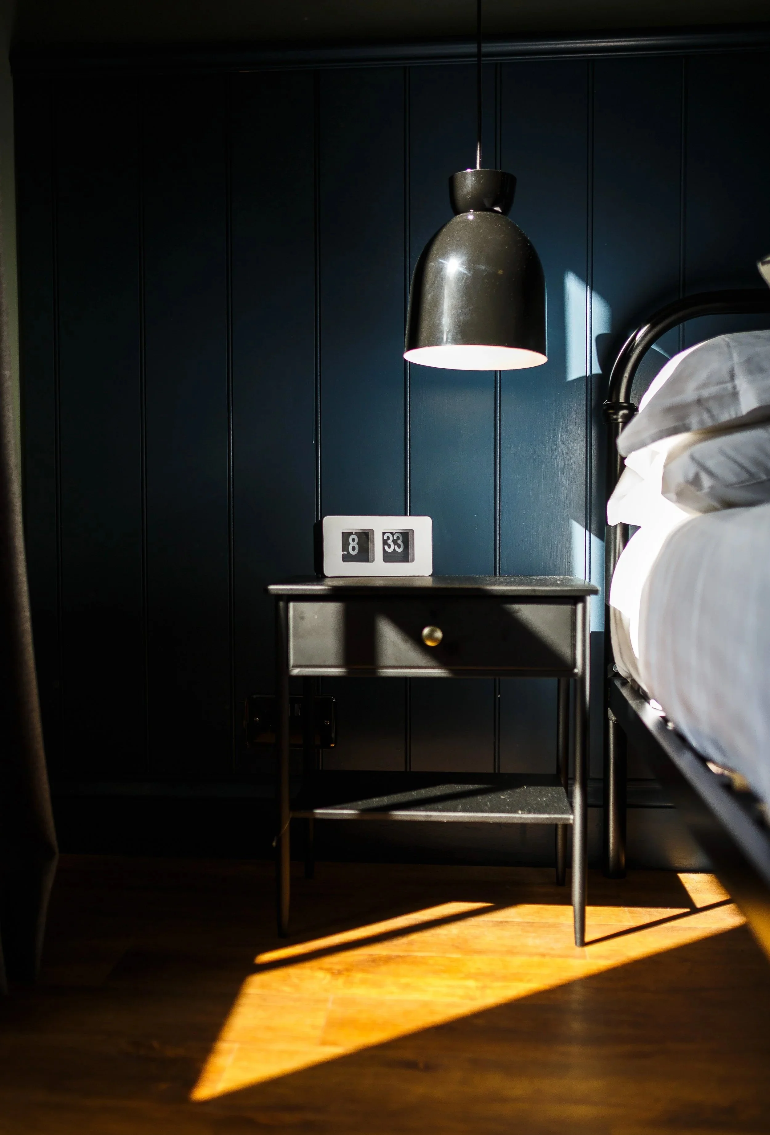 Contemporary bedroom design for a country holiday home in Anglesey by Stiwdio Interior Design. Deep blue panelled walls, heritage-inspired detailing and soft coastal light create a calm, timeless retreat that reflects the landscape and traditional ch
