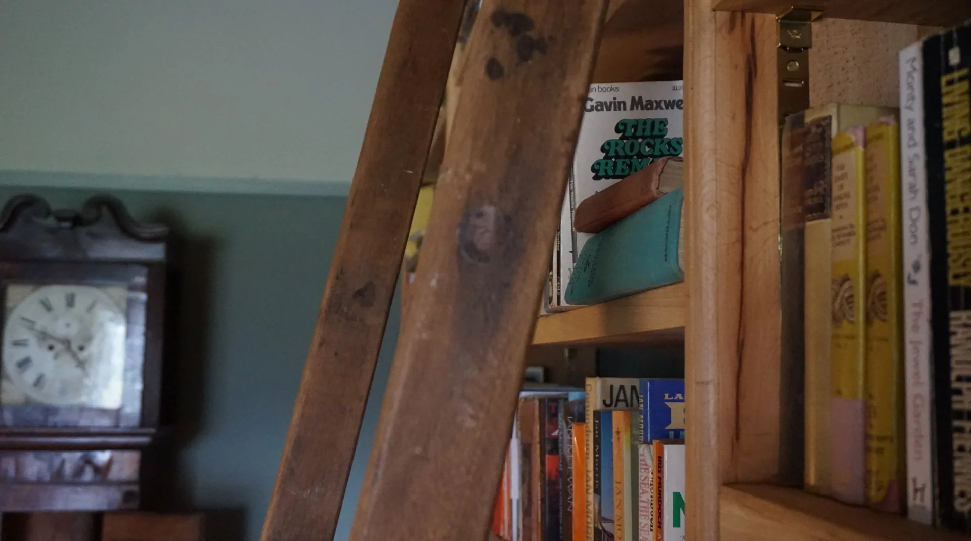 Bespoke library corner featuring a timber ladder, curated book collection and antique clock, part of a country house refurbishment in Anglesey, North Wales by Stiwdio Interior Design, blending heritage character with relaxed, layered interiors.