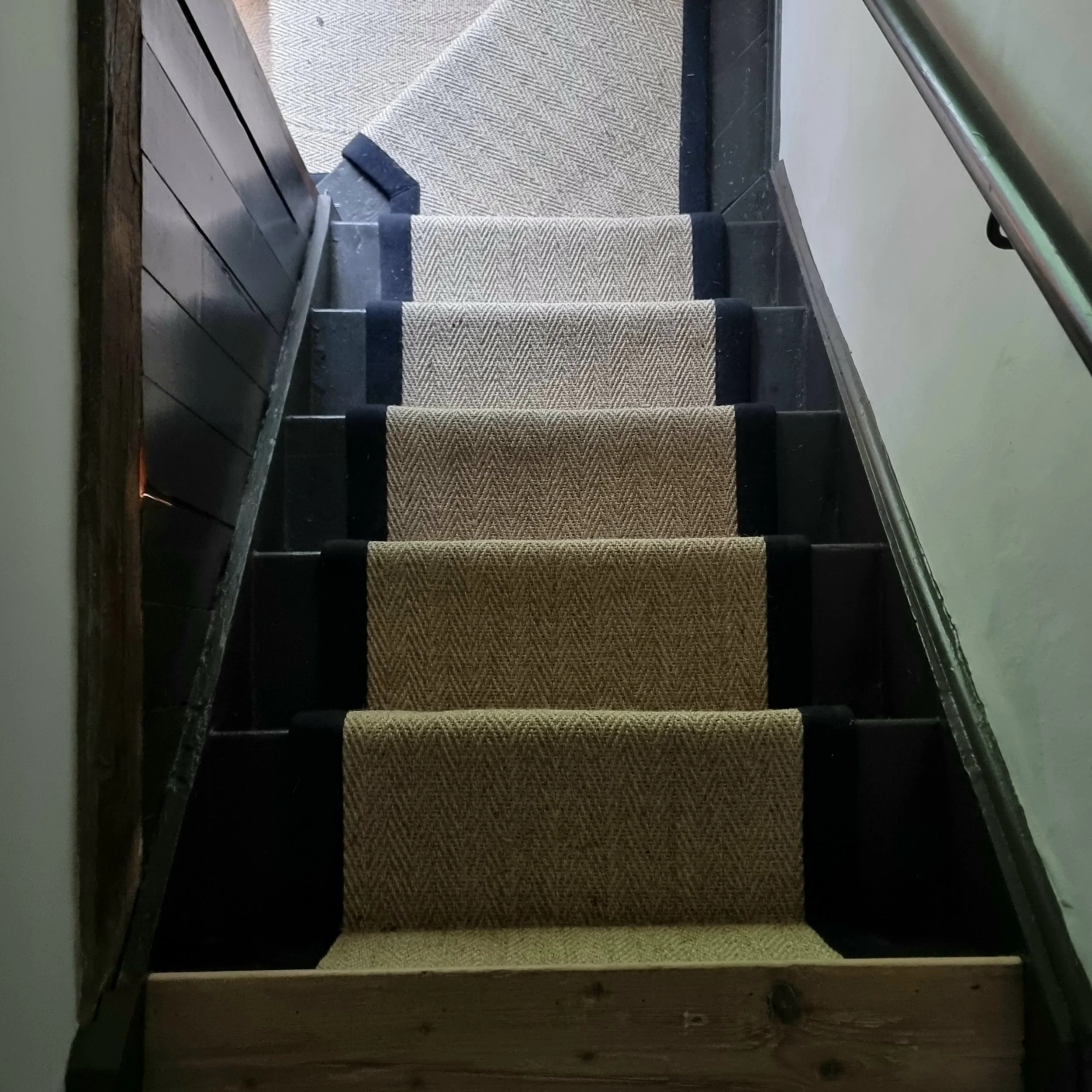 Staircase with coir or jute carpet runners and black edges, leading upstairs in a building.