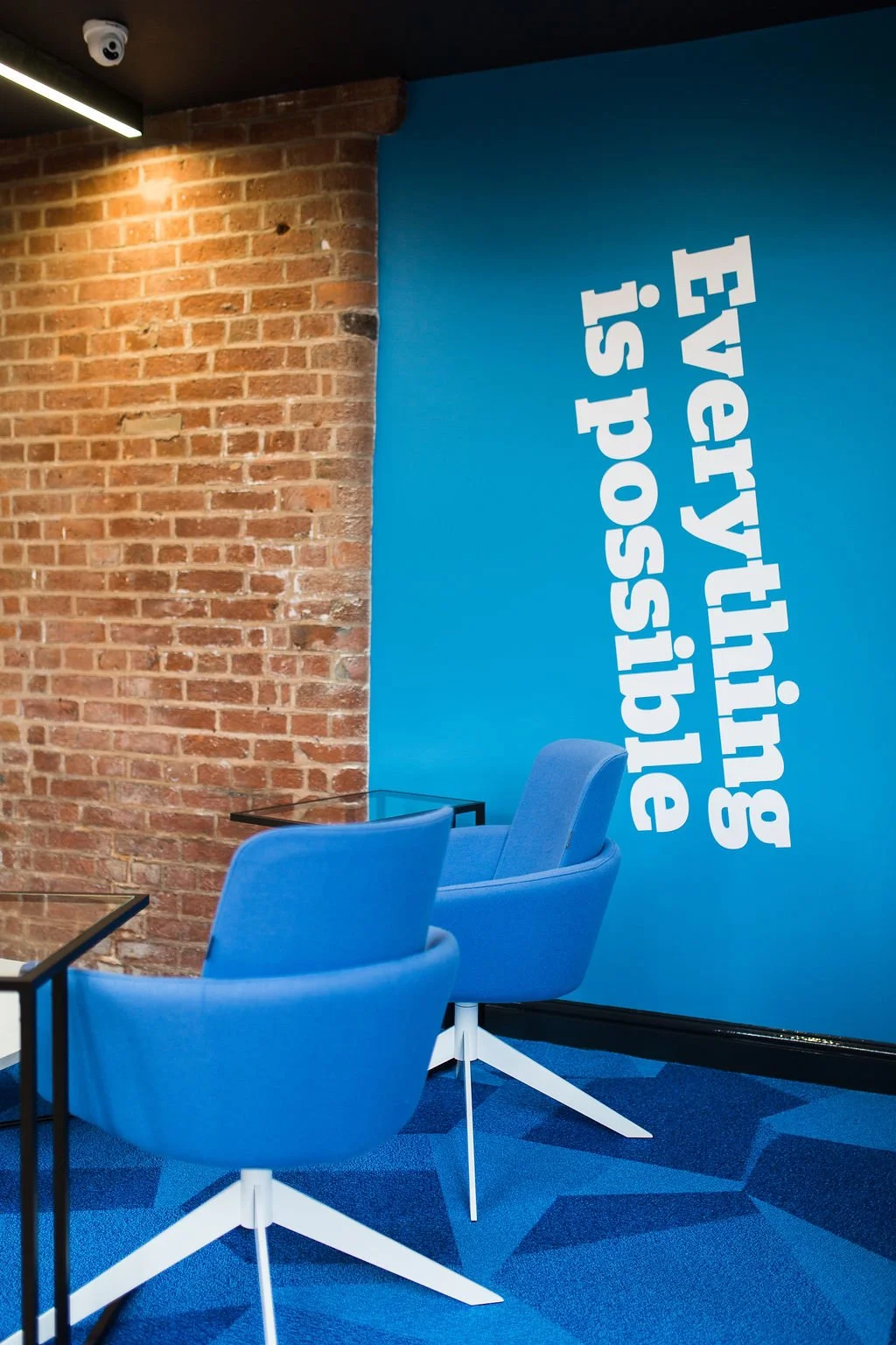 Branded breakout space within a heritage mill office refurbishment, combining exposed brickwork with bold graphic walls and contemporary seating—commercial office interior design by Stiwdio, North Wales specialists in creative workspace design and ad