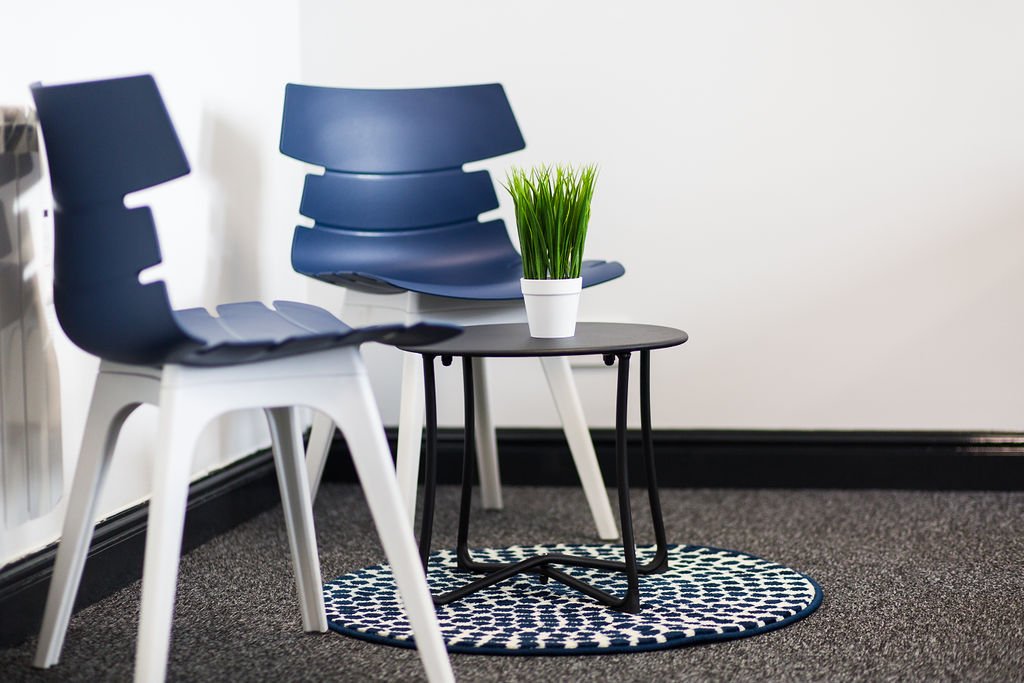 Contemporary breakout seating area within a heritage office refurbishment, designed by Stiwdio Interior Design, North Wales. Featuring modern blue and white chairs, a minimalist black side table and graphic circular rug, this commercial interior bala