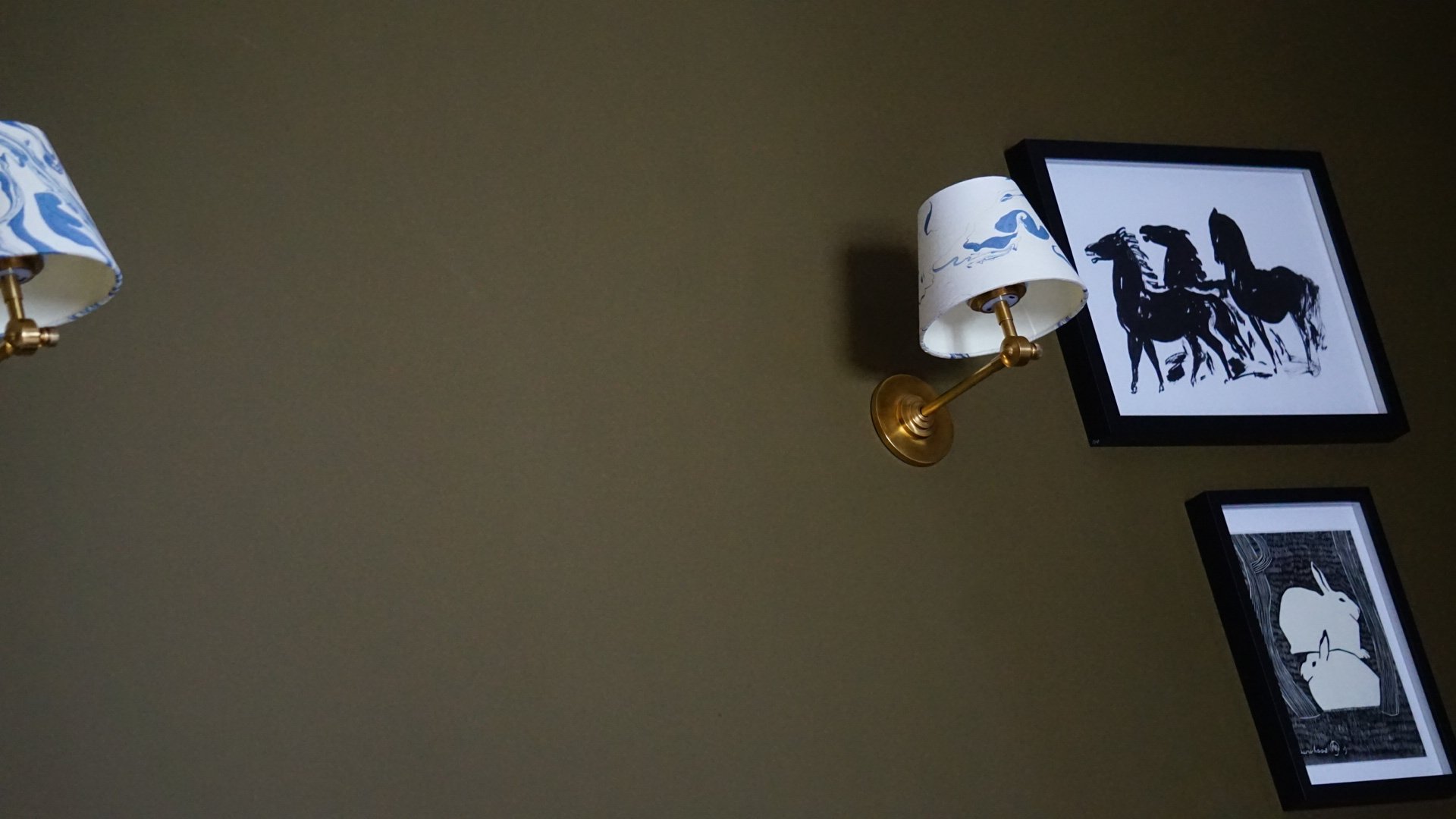 Detail of olive-green Georgian bedroom wall with brass wall lights, patterned fabric shades and black-framed monochrome artwork, designed by Stiwdio Interior Design in Liverpool.