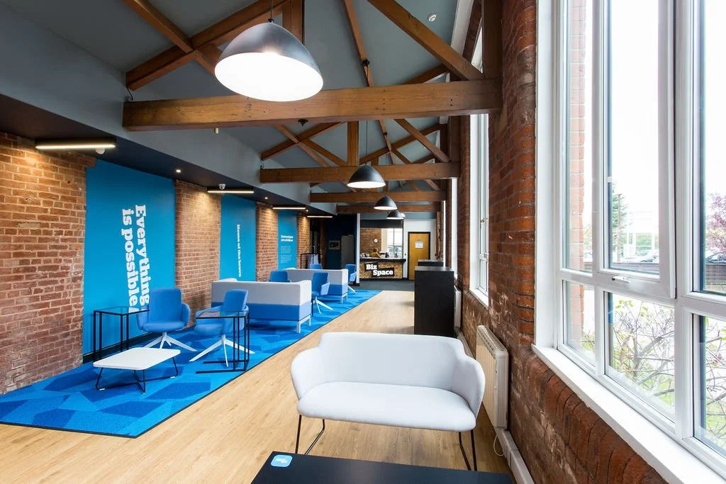 Heritage office refurbishment in a former Manchester mill, featuring exposed brick, timber trusses and modern breakout spaces by Stiwdio Interior Design, North Wales commercial interior specialists.