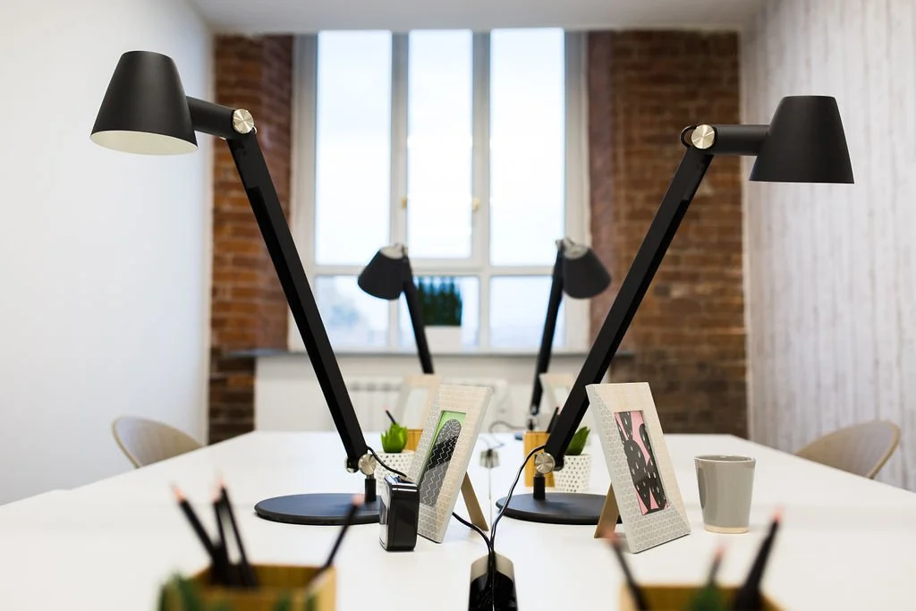 Modern co-working desk space within a heritage mill office refurbishment, designed by Stiwdio Interior Design, North Wales. Featuring clean white workstations, black adjustable task lighting and exposed brick walls, this commercial interior blends in