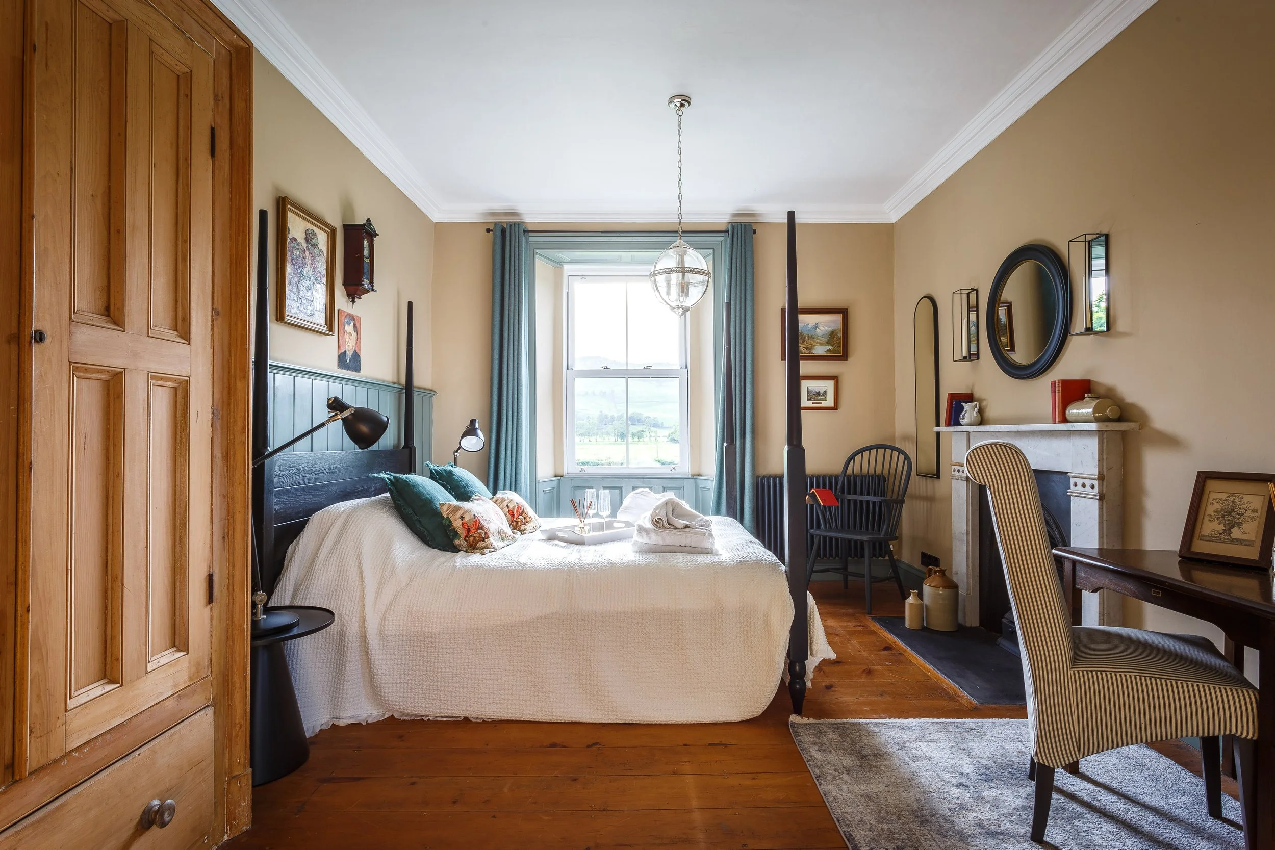 Elegant country house bedroom renovation with four-poster bed, original fireplace and countryside views, combining period features and soft heritage colours in a timeless North Wales interior.