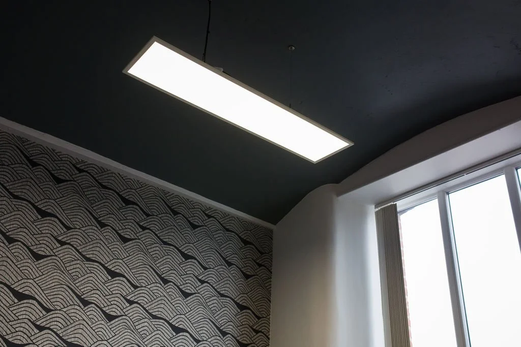 Contemporary office meeting space within a converted mill building, featuring graphic monochrome wallpaper, a bold painted ceiling and streamlined suspended lighting. Designed by Stiwdio, North Wales, this heritage-led commercial interior balances or