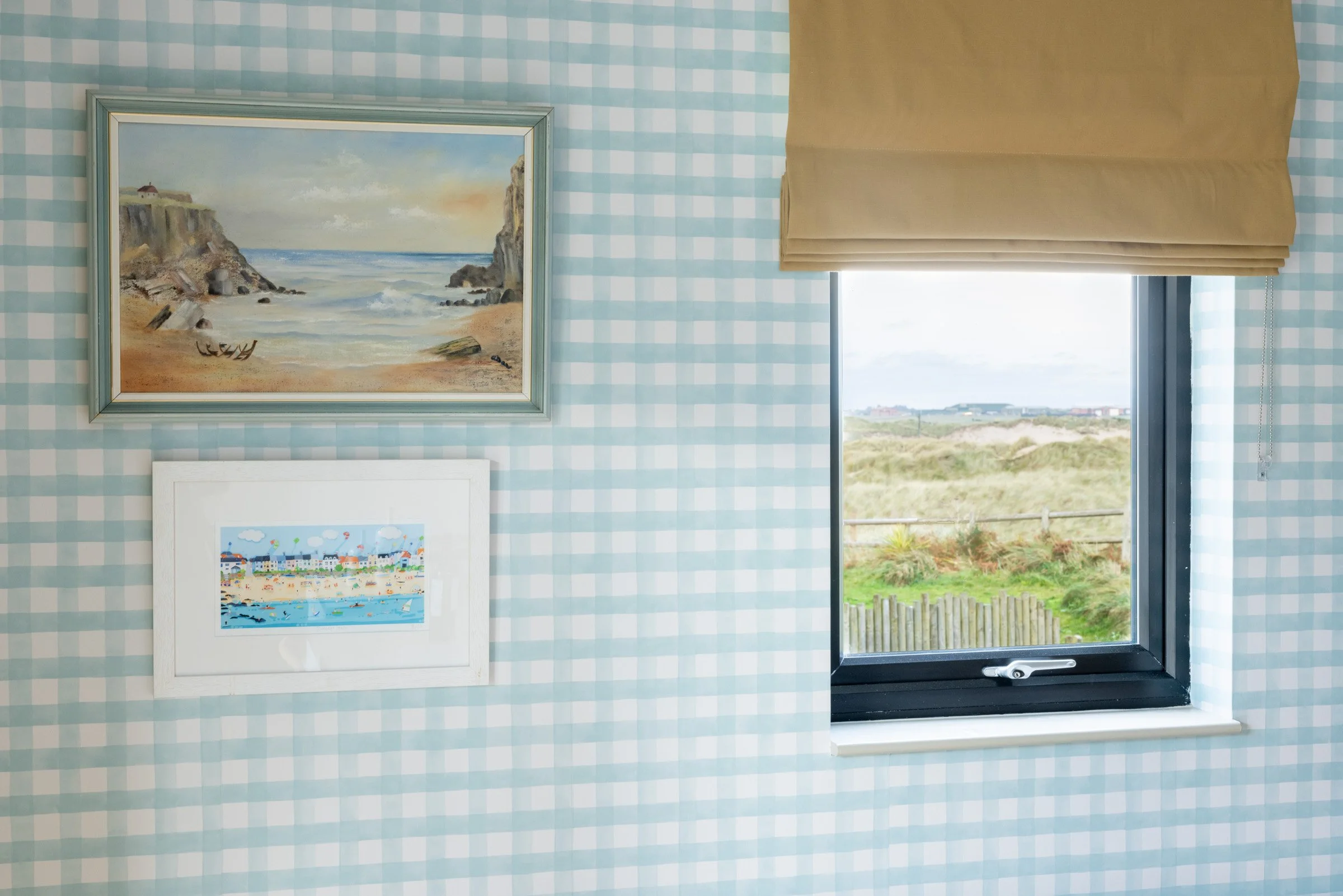 Beach hut-inspired interior in a Rhosneigr holiday let featuring coastal artwork, soft blue gingham walls and dune views in Anglesey.