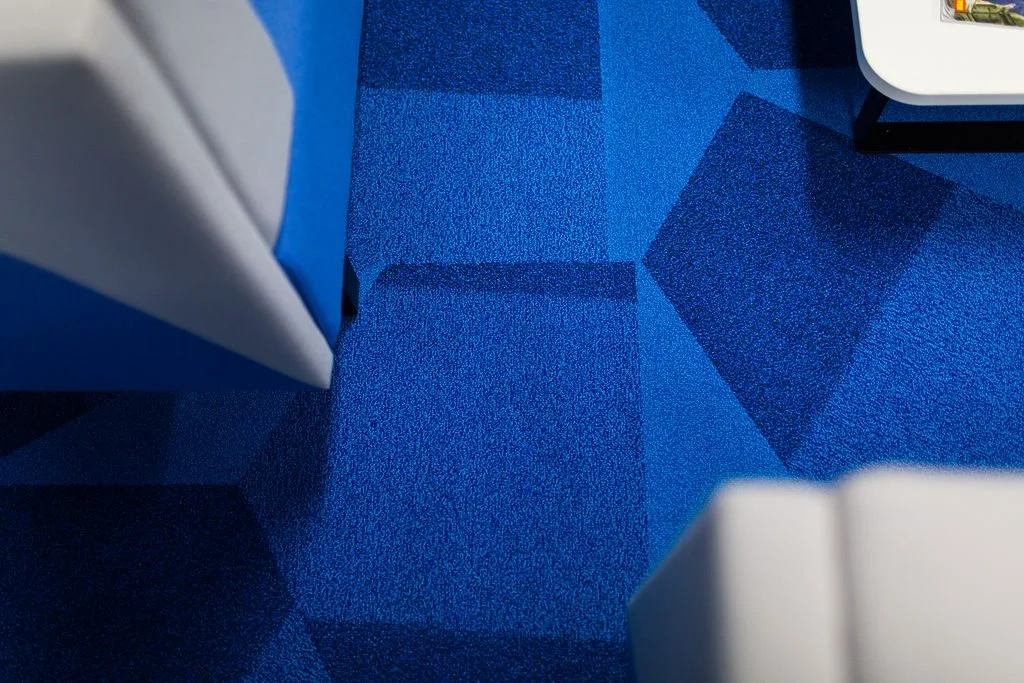 Geometric blue carpet design within a heritage mill office refurbishment, creating dynamic zoning in collaborative workspaces. Commercial interior design by Stiwdio, North Wales—specialists in modern office environments that respect historic architec
