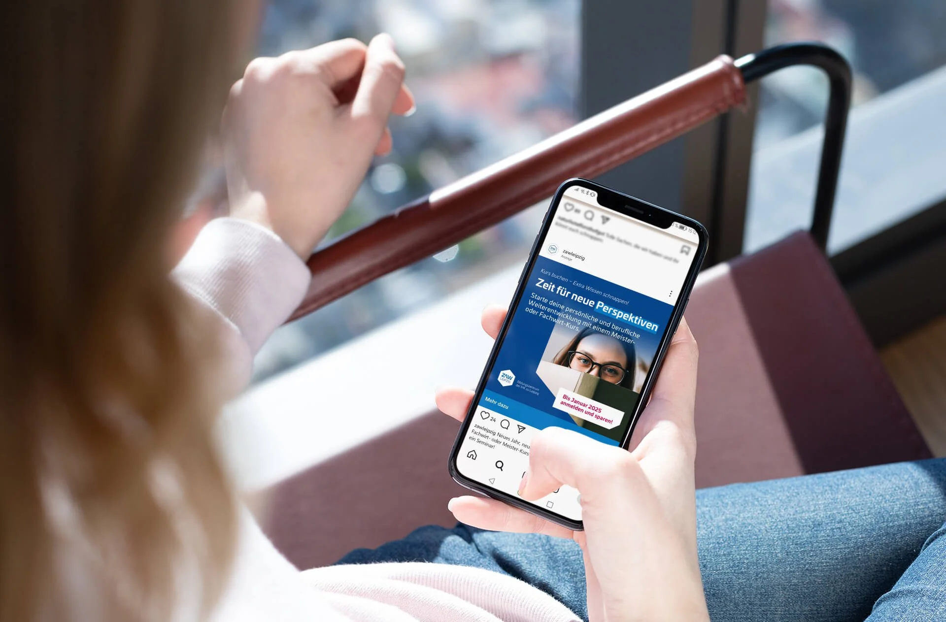 Eine Hand hält ein Handy auf dem ein vom MarkOp Studio gestalteter Social Media Post der ZAW Leipzig geöffnet ist.