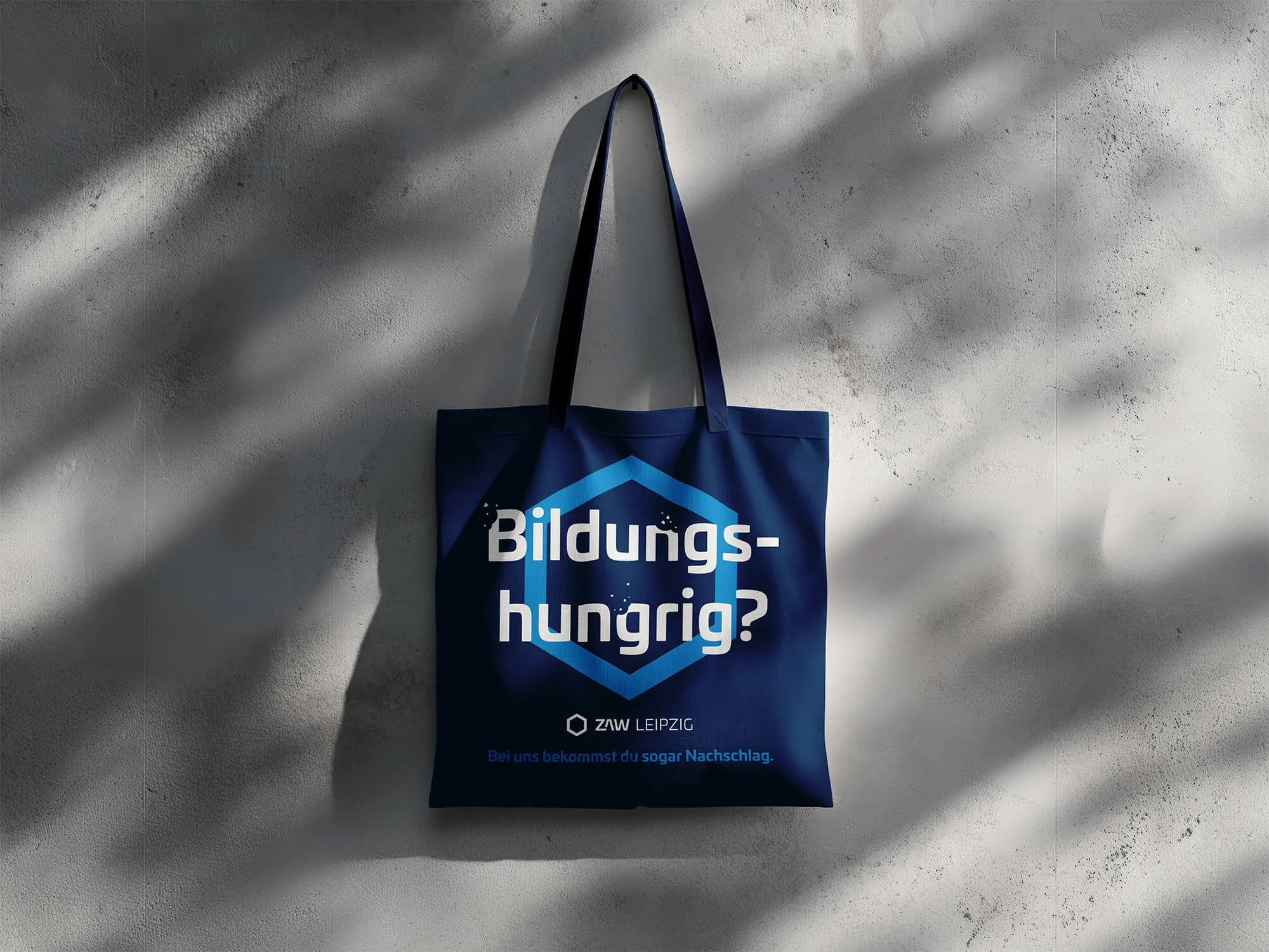 Ein blauer Beutel mit der Aufschrift Bildungshungrig? hängt vor einer grauen Wand.