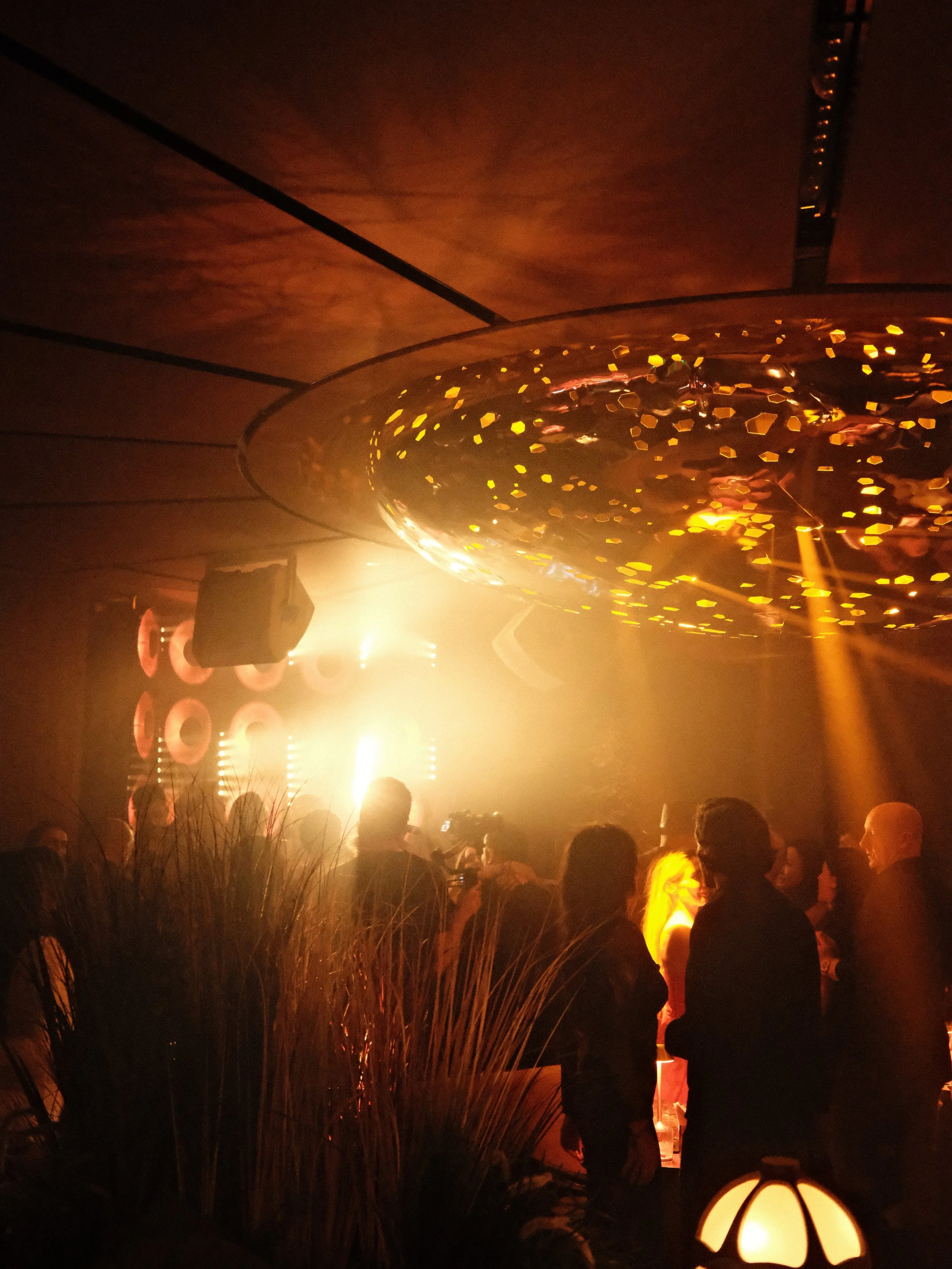 Image of people in the CASA NEOS Lounge, with the lights from the DJ booth shining orange into the crowd.