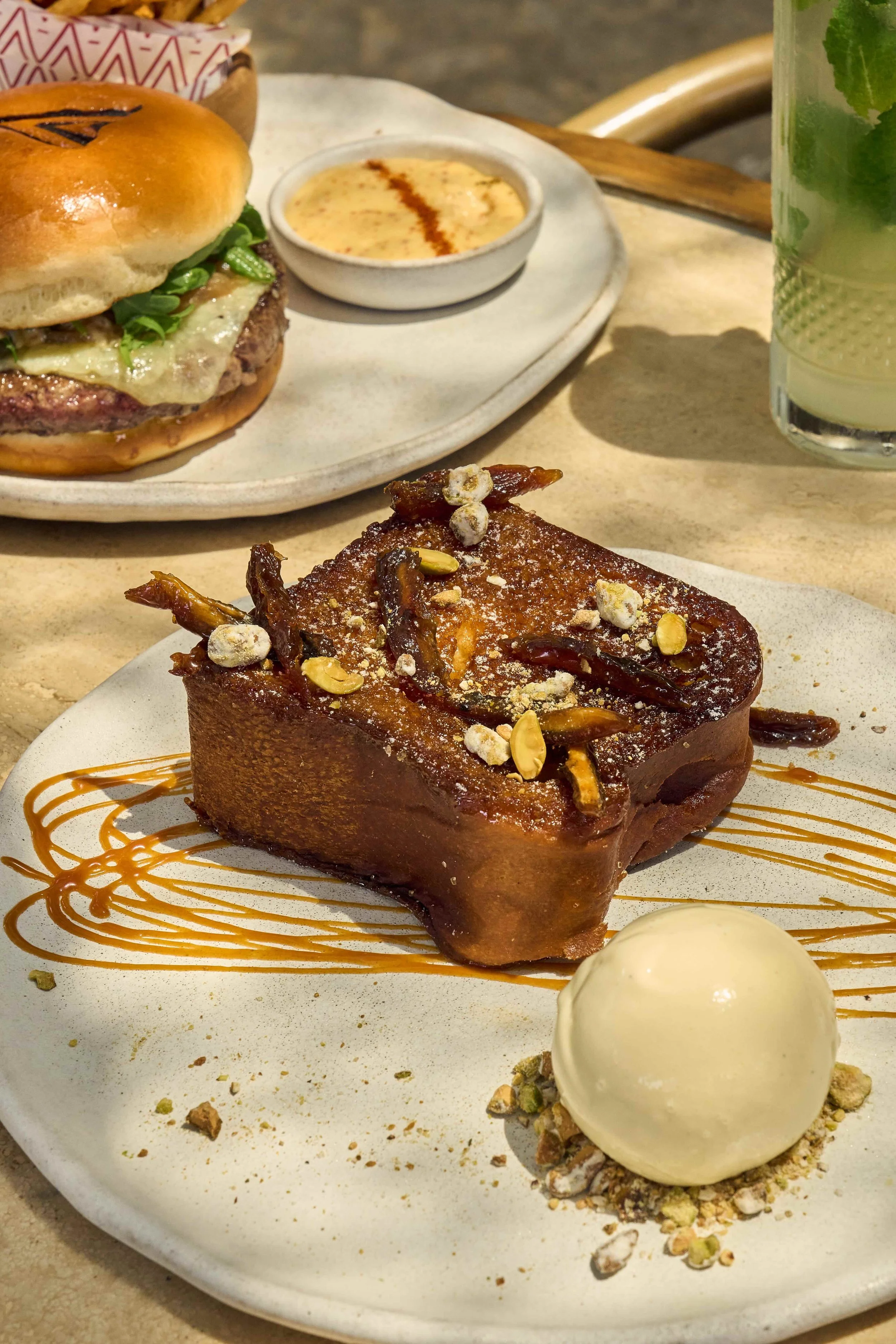 Delicious Pain Perdu with a side of ice cream and caramel drizzle and the brunch burger on a table at CASA NEOS for brunch.