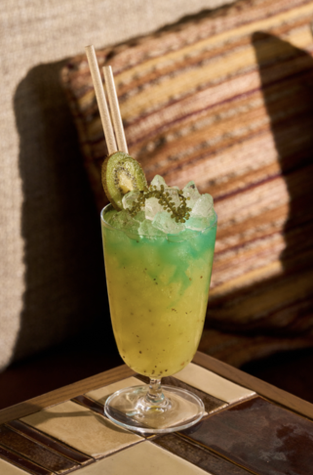 A vibrant yellow and green cocktail, garnished with Kiwi at CASA NEOS brunch.