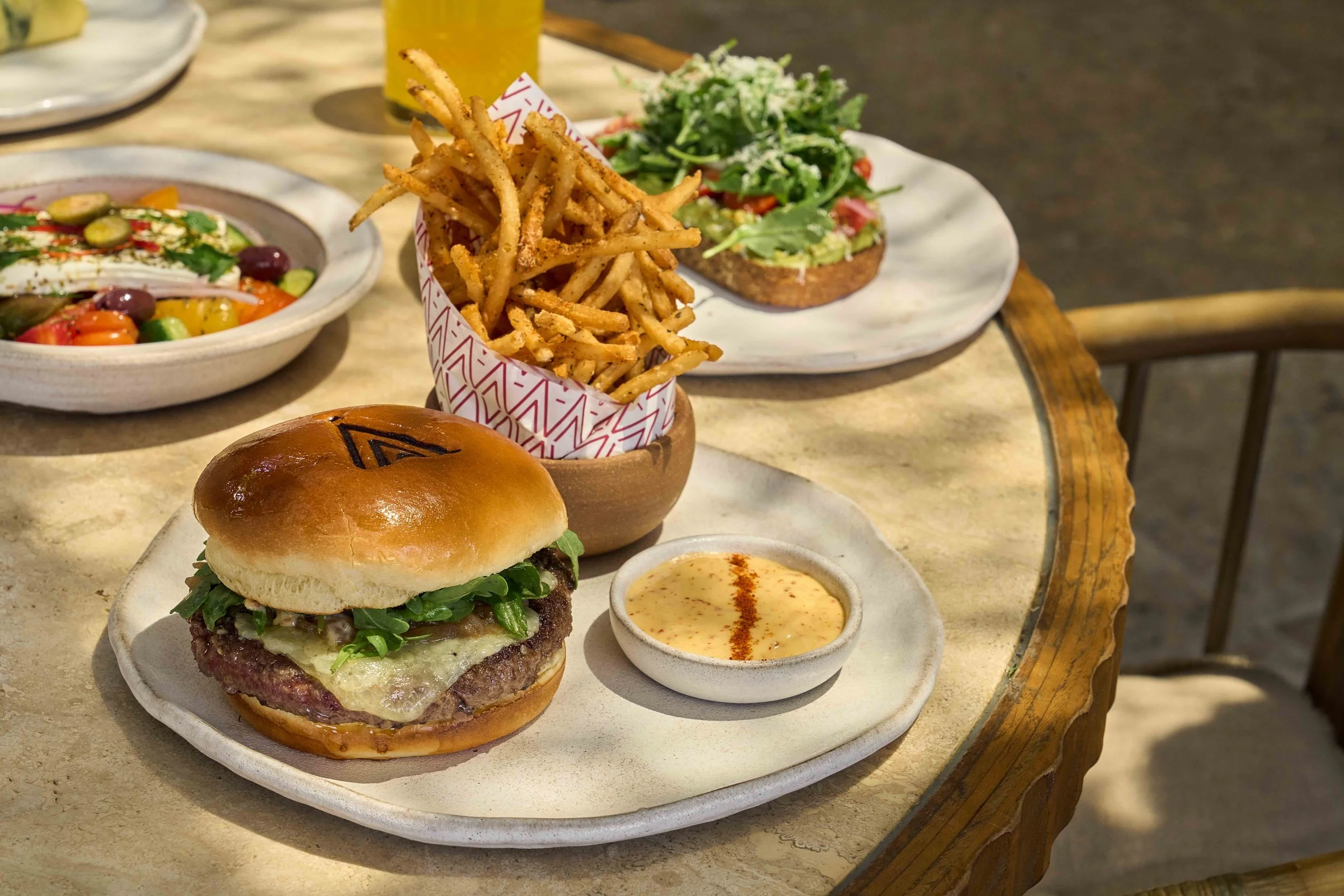 A brunch burger with the AVA logo on the bun, with a side of fries and burger sauce.