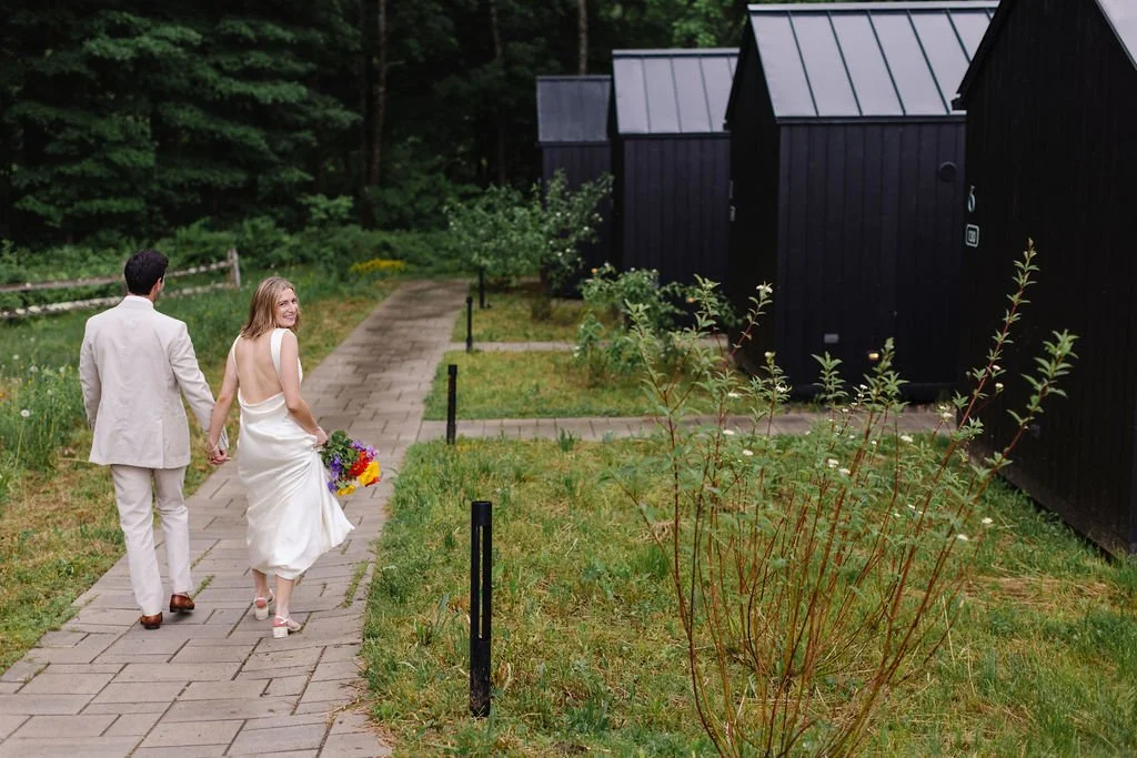 Bride and groom kissing during outdoor wedding ceremony, guests clapping and smiling, colorful flower decorations, grassy area with flower petals scattered.