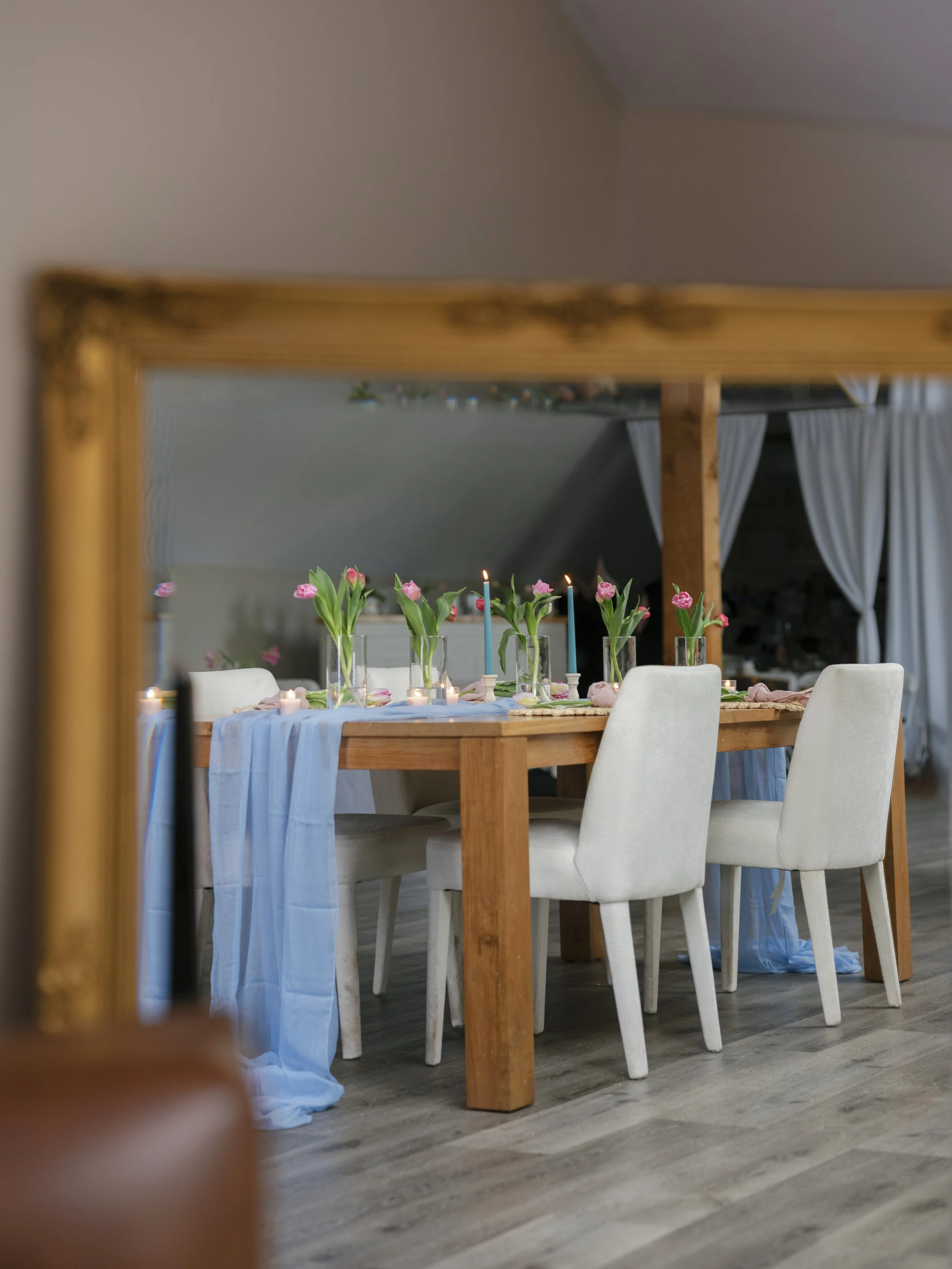 Elegant dining table set with tall glass candle holders, floral centerpieces, glasses of water, and a dark, warmly lit ambiance.