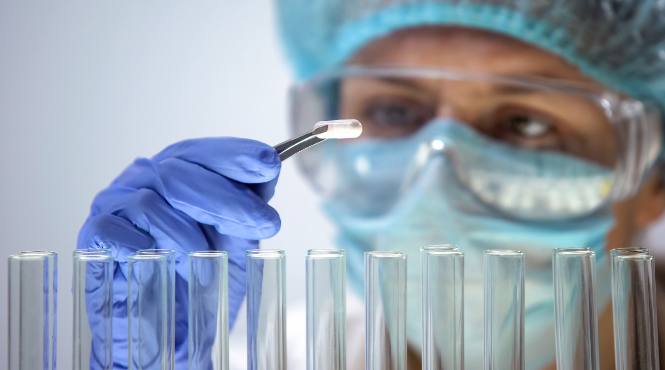 Pharmacist holding a pill with tweezers above glass tubes