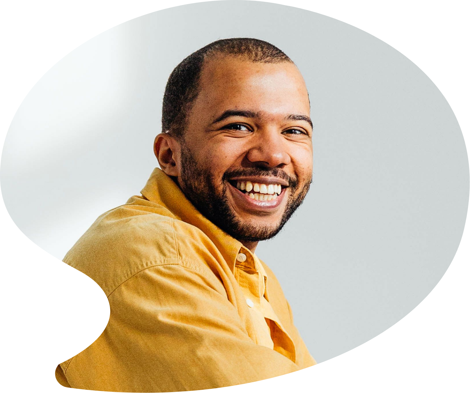 A smiling man with a beard, wearing a yellow jacket, looking over his shoulder against a light gray background.