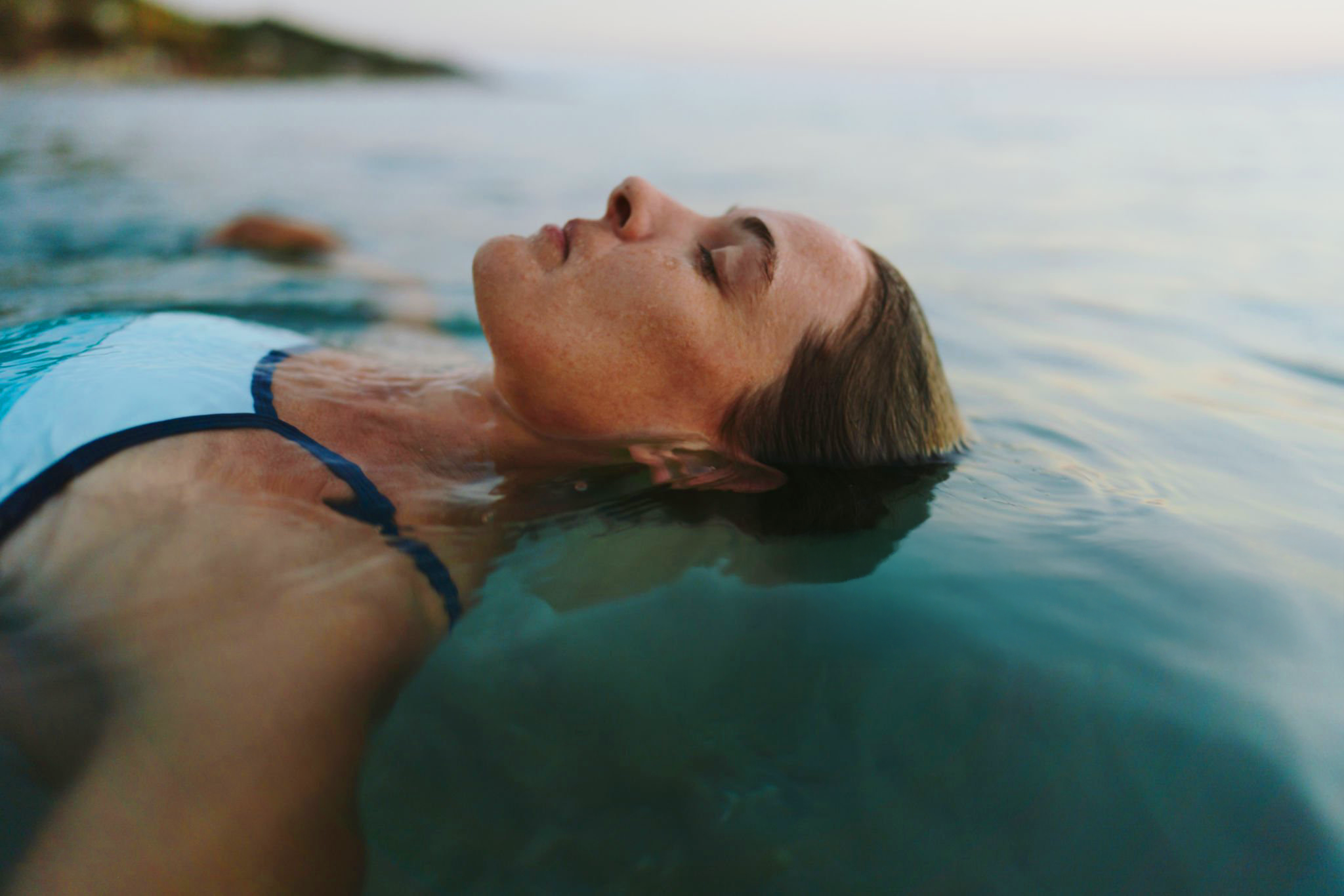 A woman with freckles and closed eyes floating on her back in a body of water, with a calm expression. Therapy in Toronto