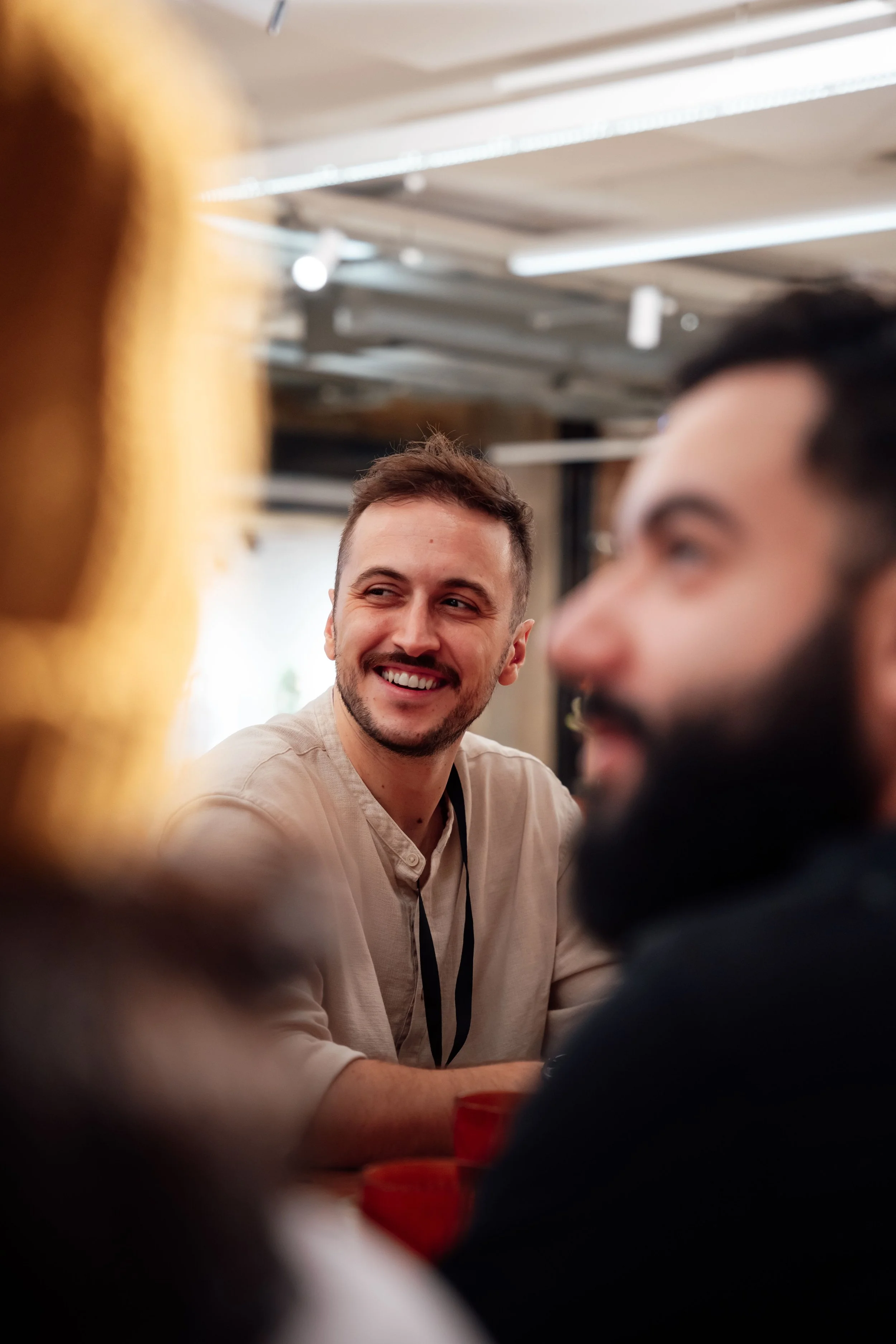 Two men sitting at a table, smiling and engaging in conversation, with a blurred background and partial view of other people's arms and hands. Trauma Therapy