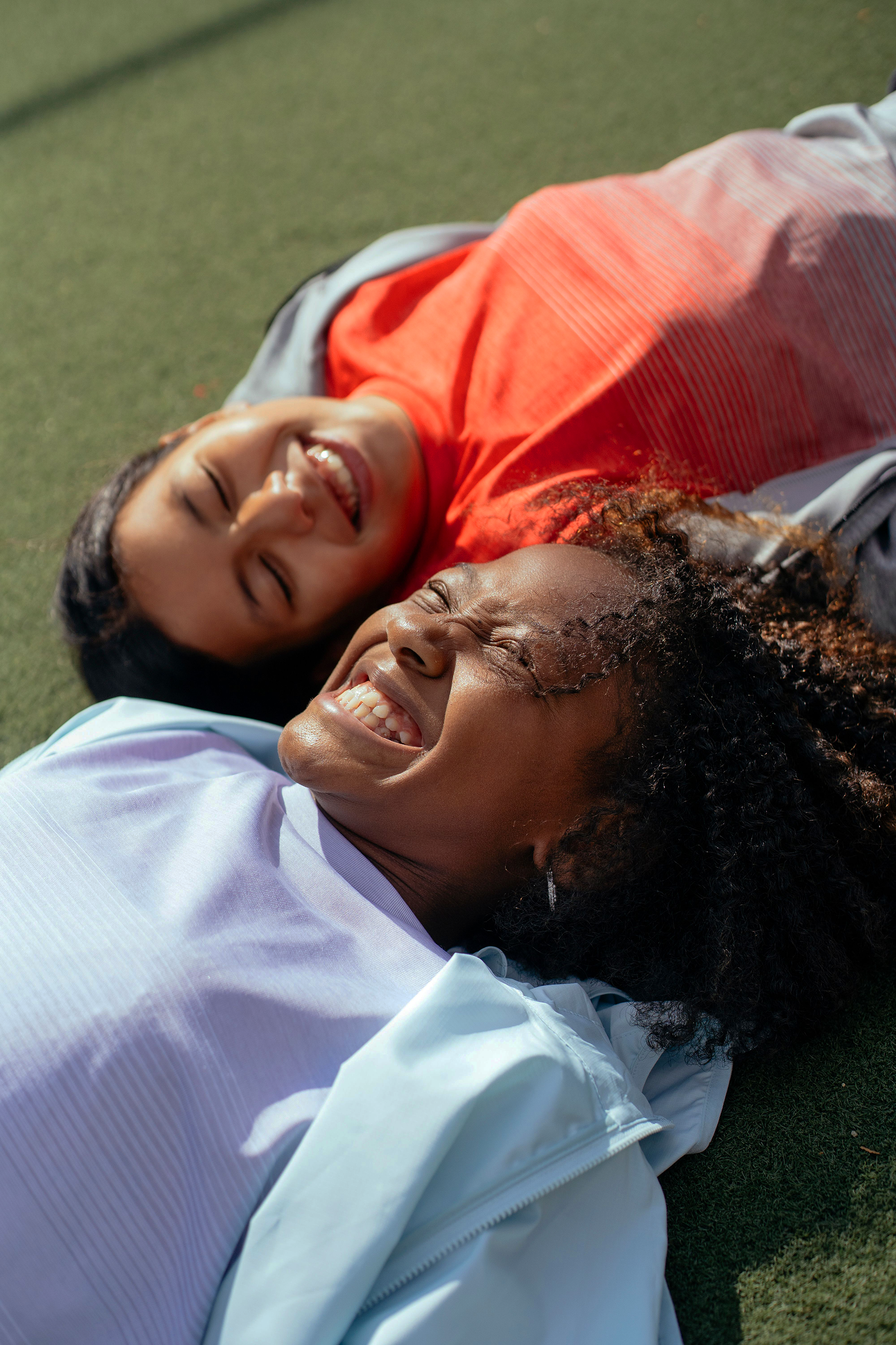 Two individuals lying on the grass and smiling, with expressions of joy, wearing athletic clothing. Couples therapy in toronto