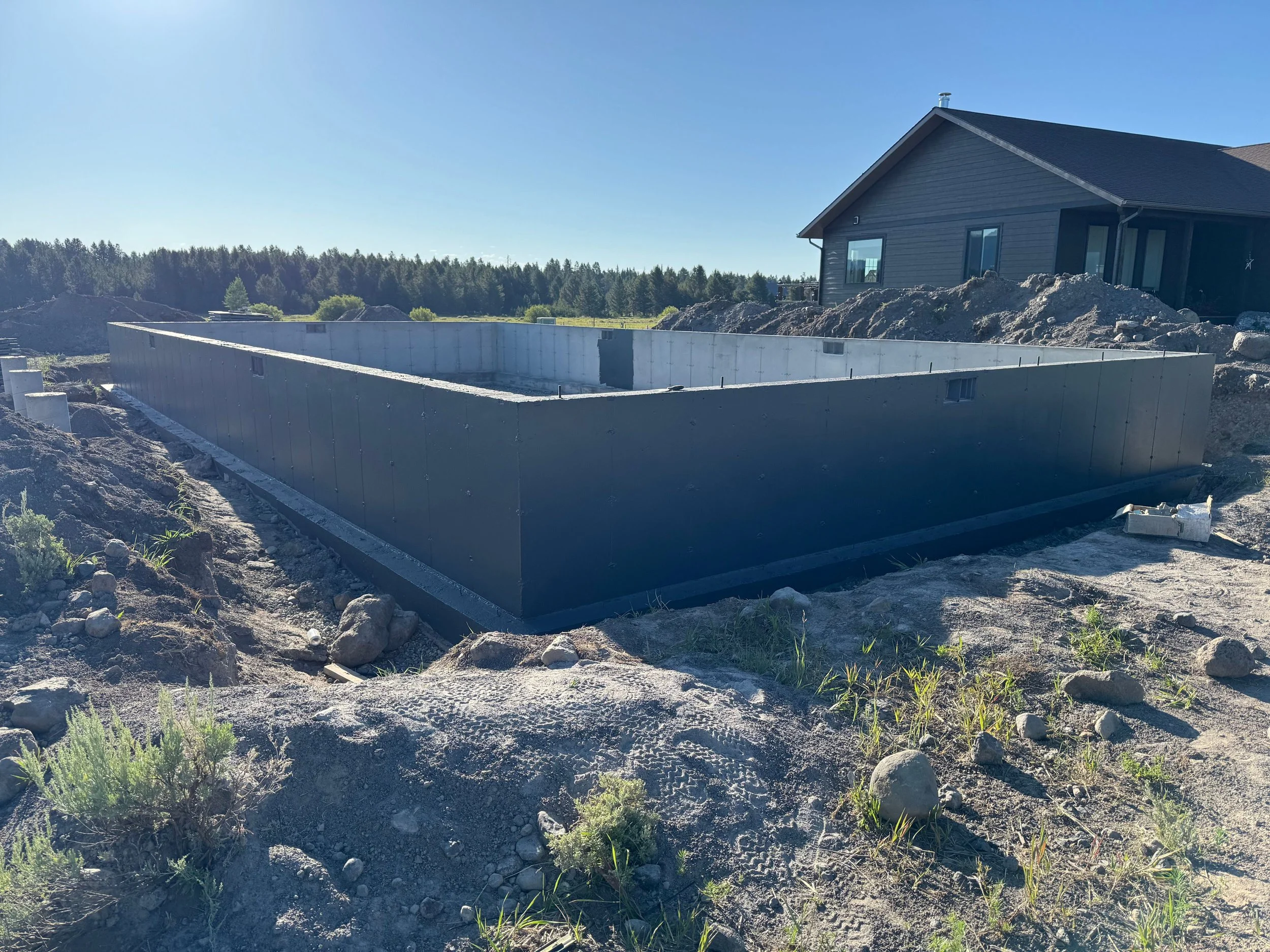 Construction site with a building foundation and a house in the background on a sunny day.
