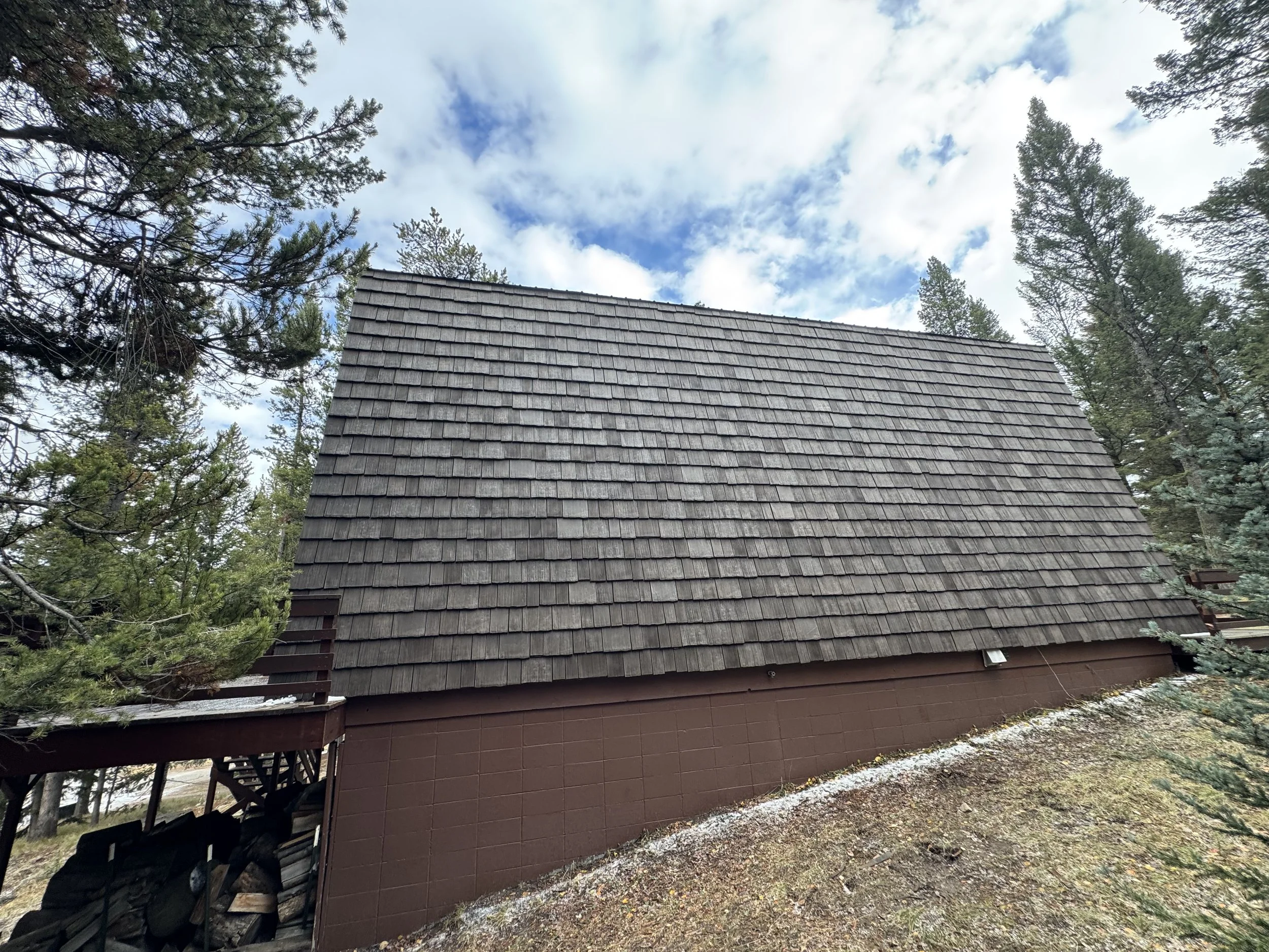 A large building with a steep, shingled roof surrounded by pine trees under a cloudy sky.