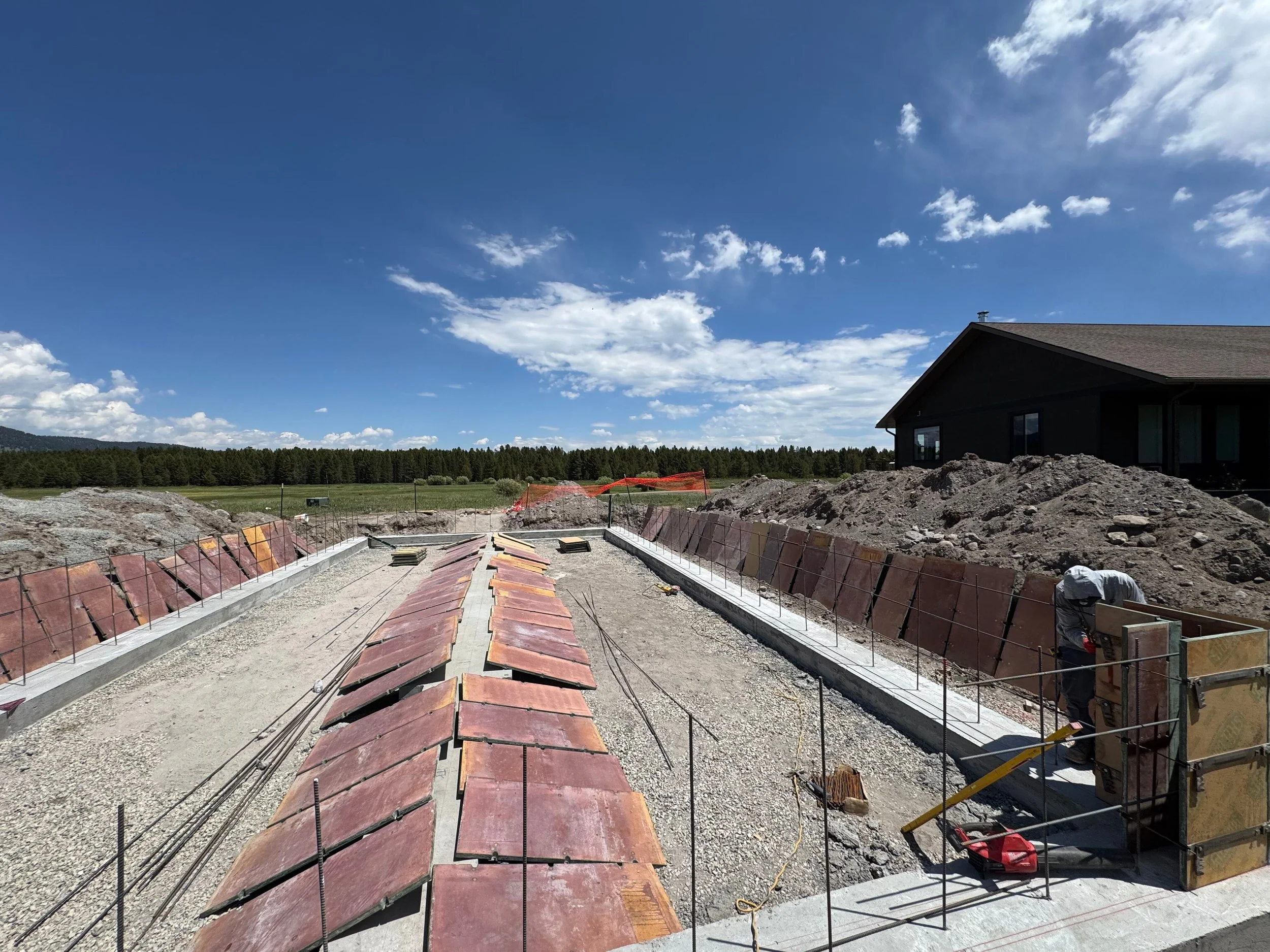 Construction site with a building foundation being prepared, with dirt piles, concrete formwork, and a clear blue sky