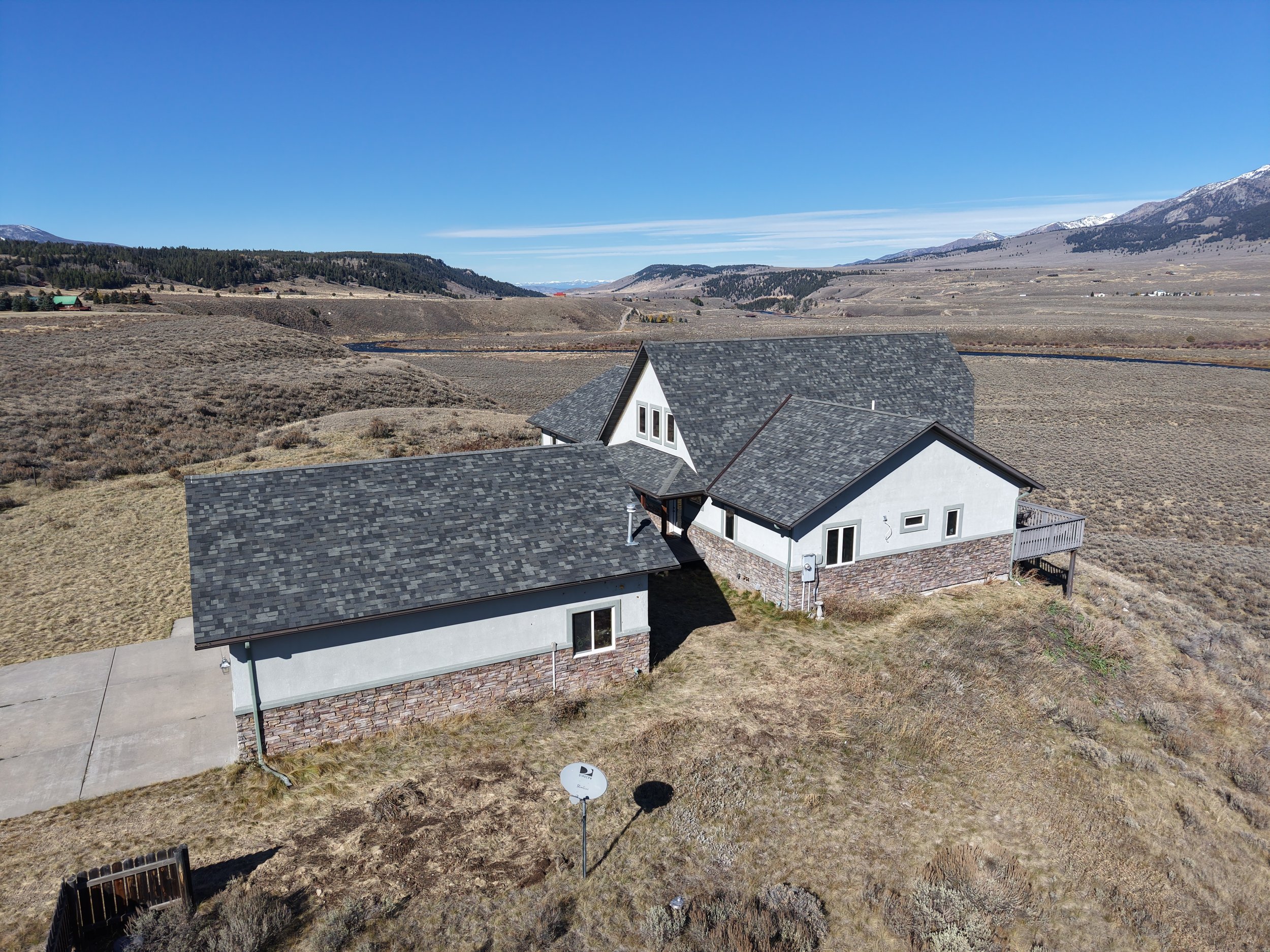 A house in a rural area with a mountainous background, a driveway, and a satellite dish, under a clear blue sky.