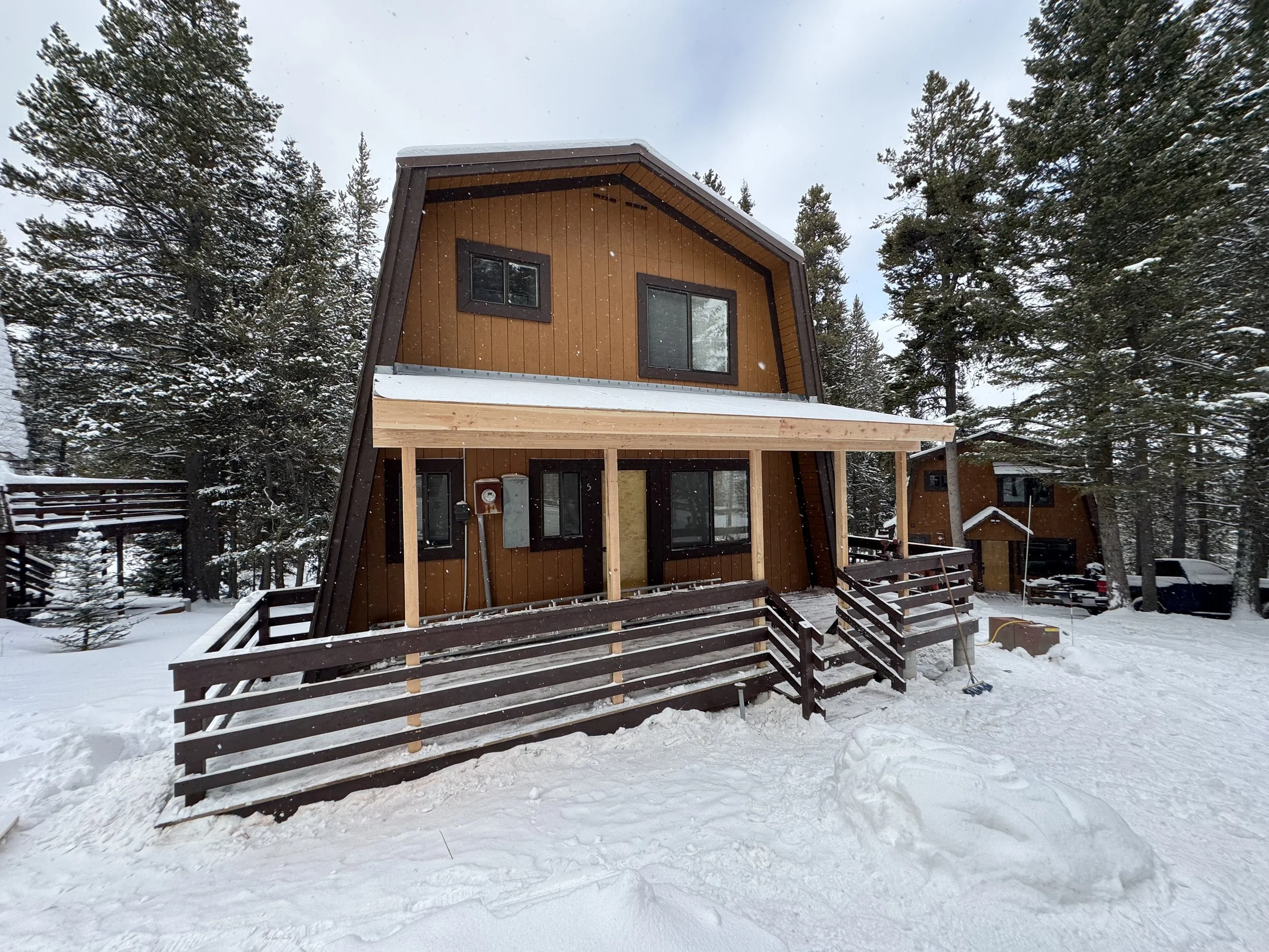 A wooden house with a dark brown exterior and a slanted roof located in a snowy forested area.
