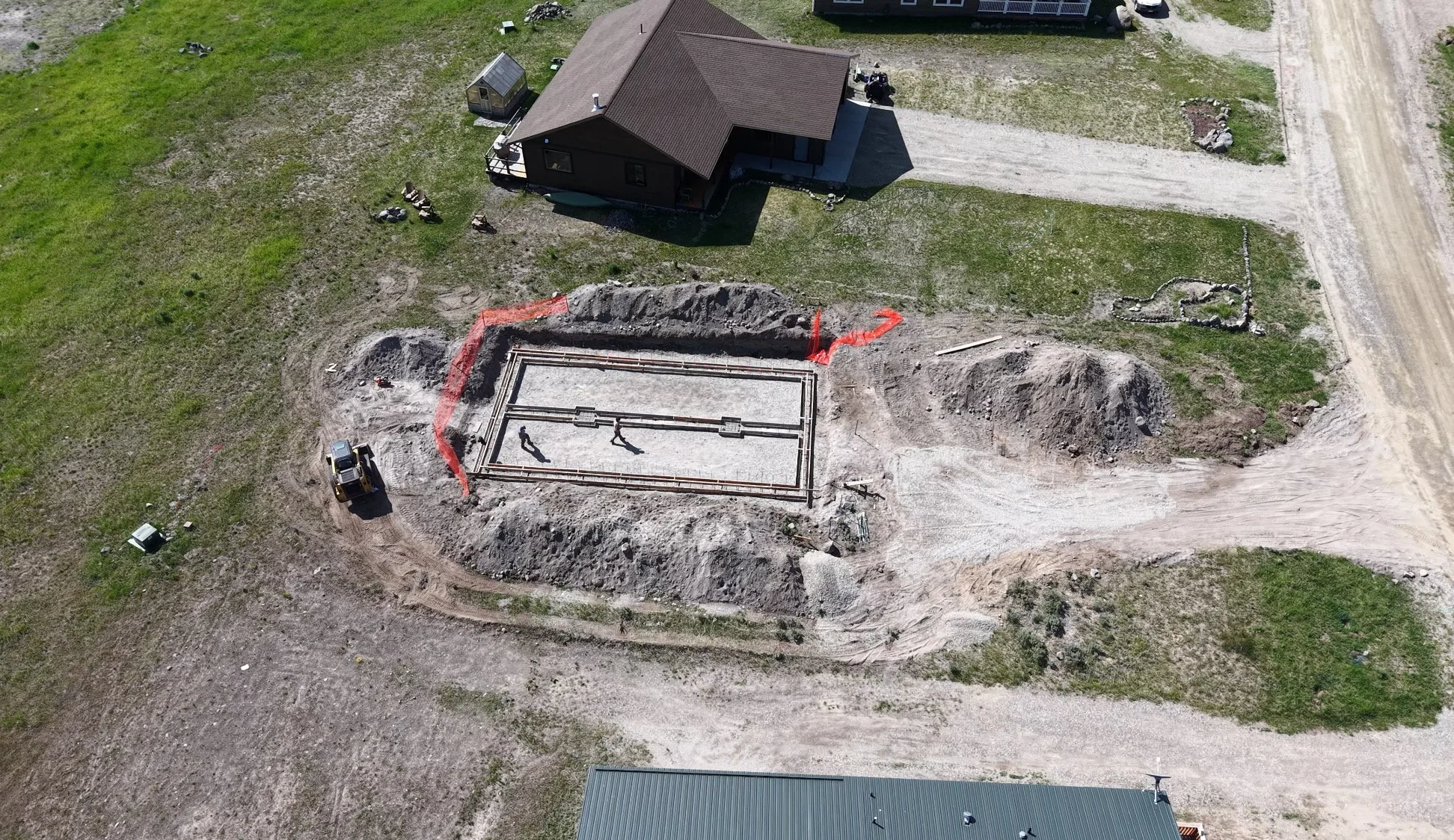 Aerial view of a house with a construction site in the front yard, showing a foundation being prepared outlined by dirt and construction equipment around it.