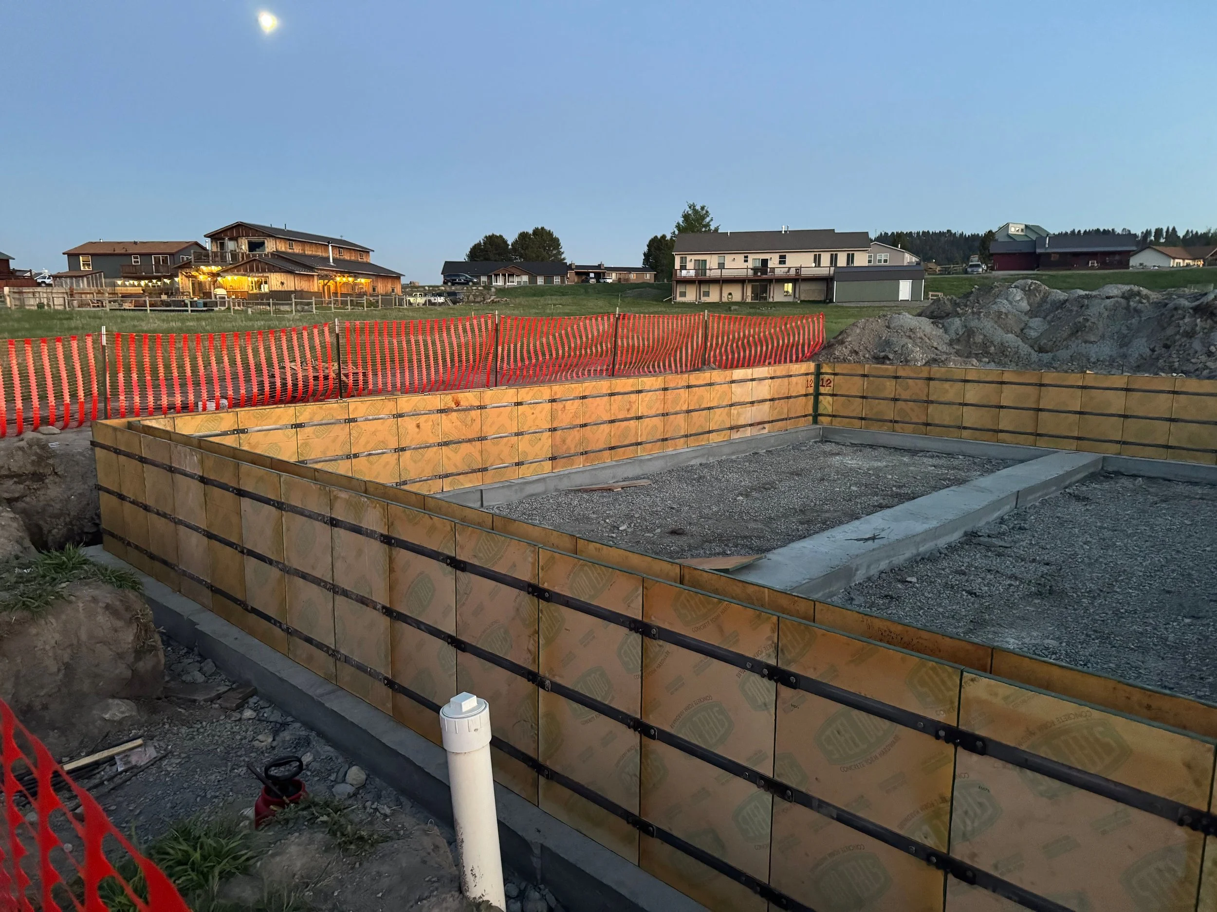 Construction site with a foundation and wooden formwork in a residential area during twilight.
