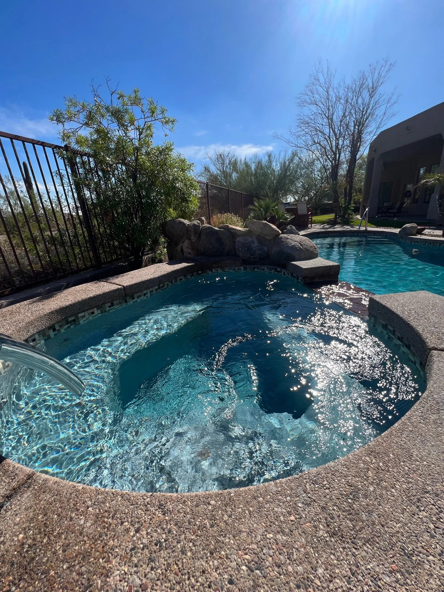 Sunlit pool and spa with natural blue water, stone edging, and desert landscaping.