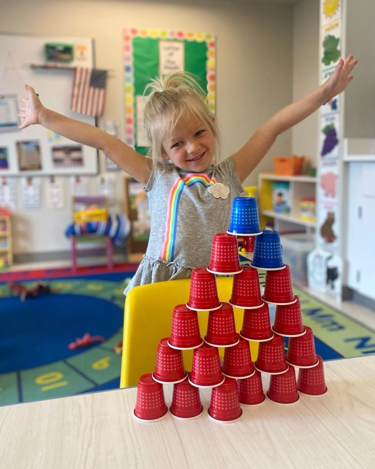 Preschool-aged girl standing excitedly behind a tower of cups she stacked.