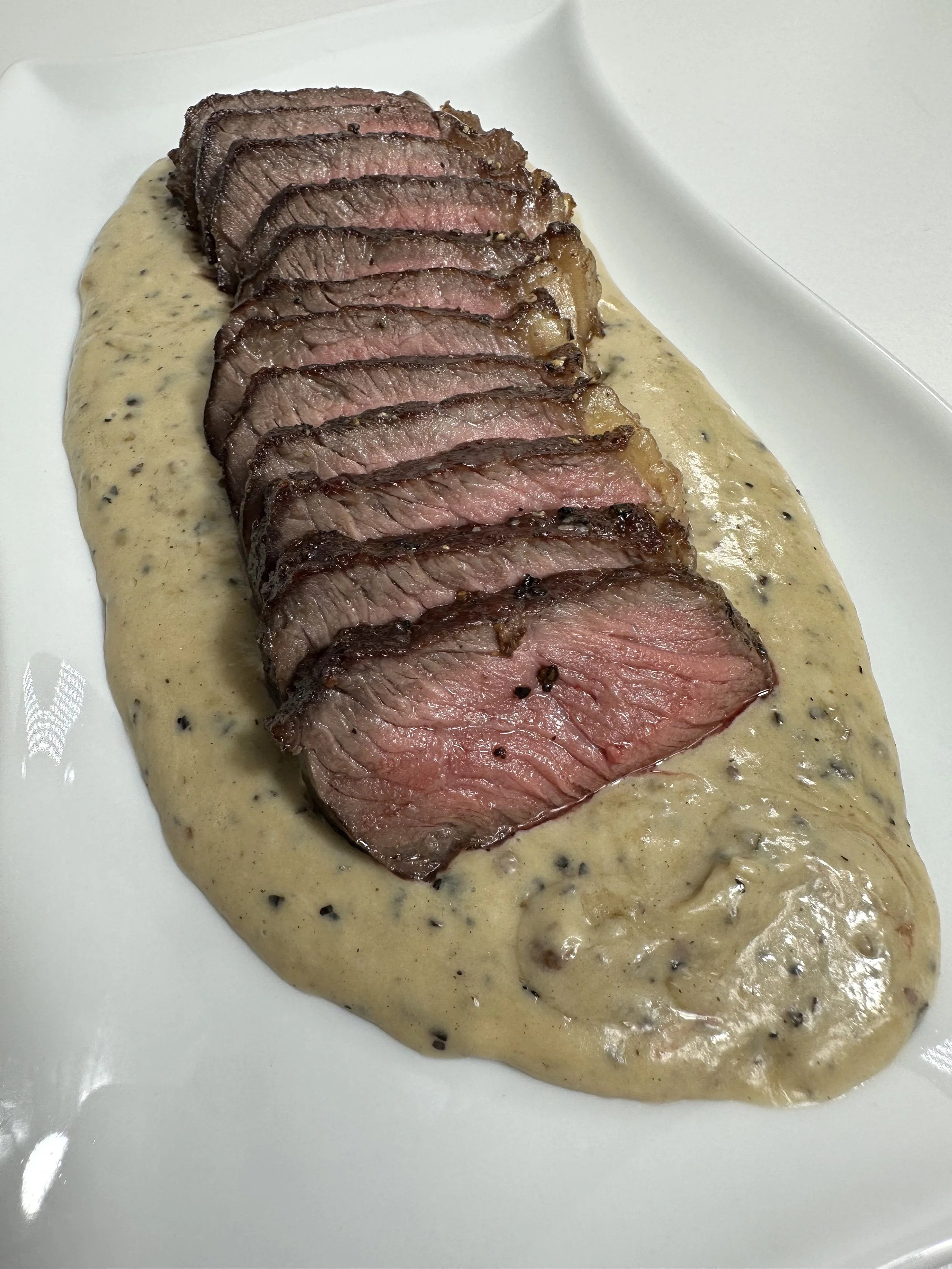 Slices of cooked steak with a pink center, laid on a creamy mustard and black pepper sauce. The meat appears tender and well-prepared.