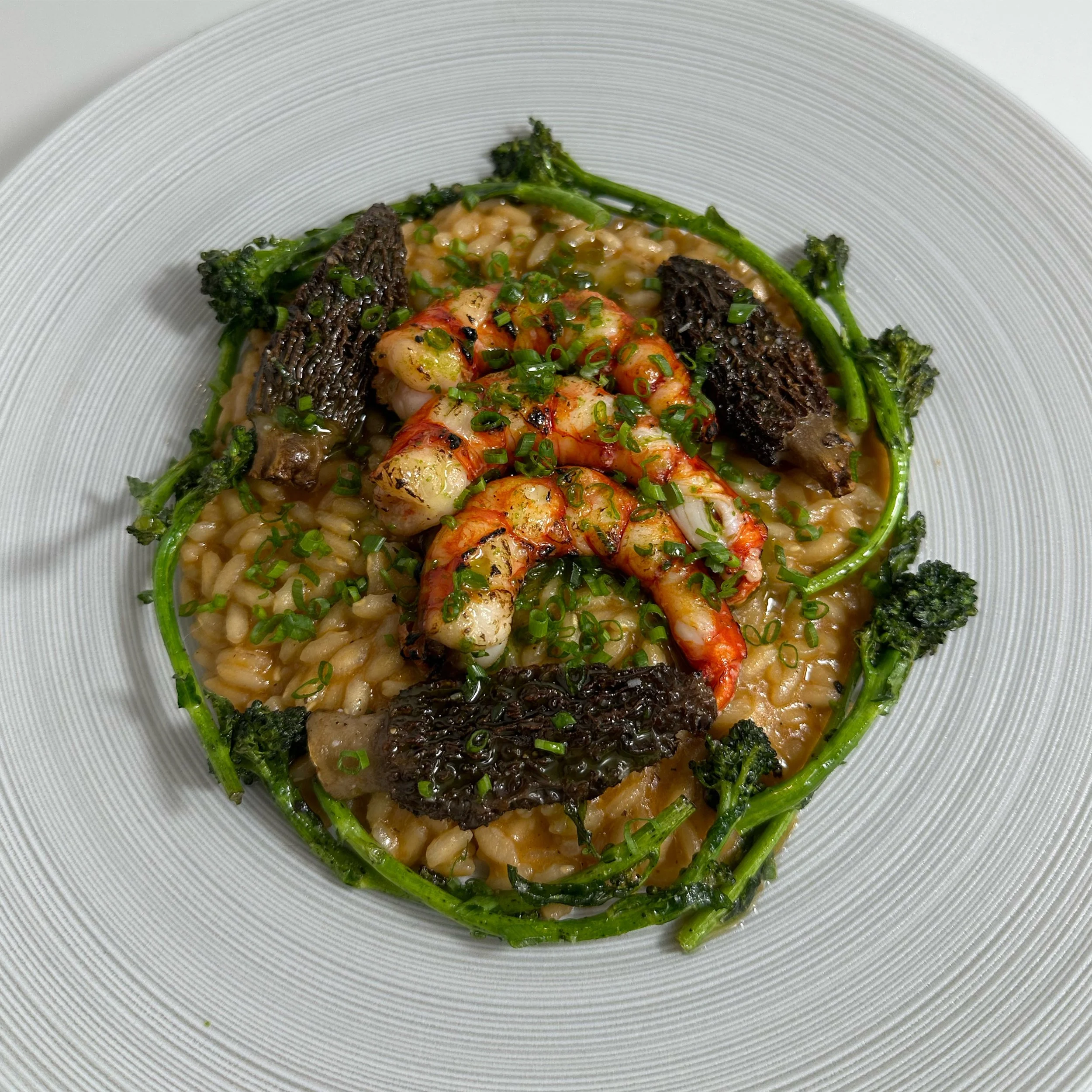 Seafood and grilled vegetable dish with rice, garnished with chopped green herbs, served on a white plate.