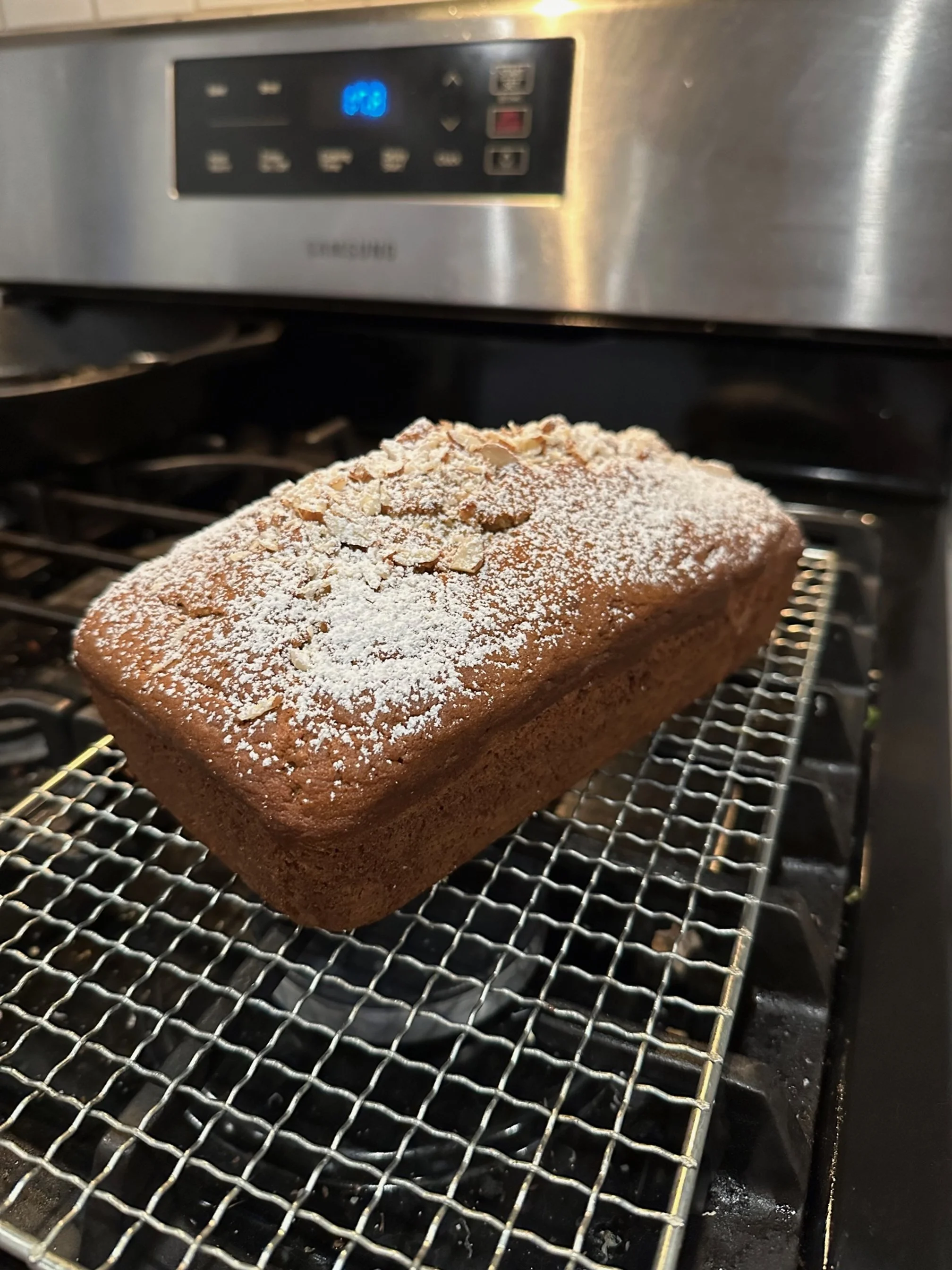 Freshly baked loaf of bread on a cooling rack in front of a stainless steel oven.