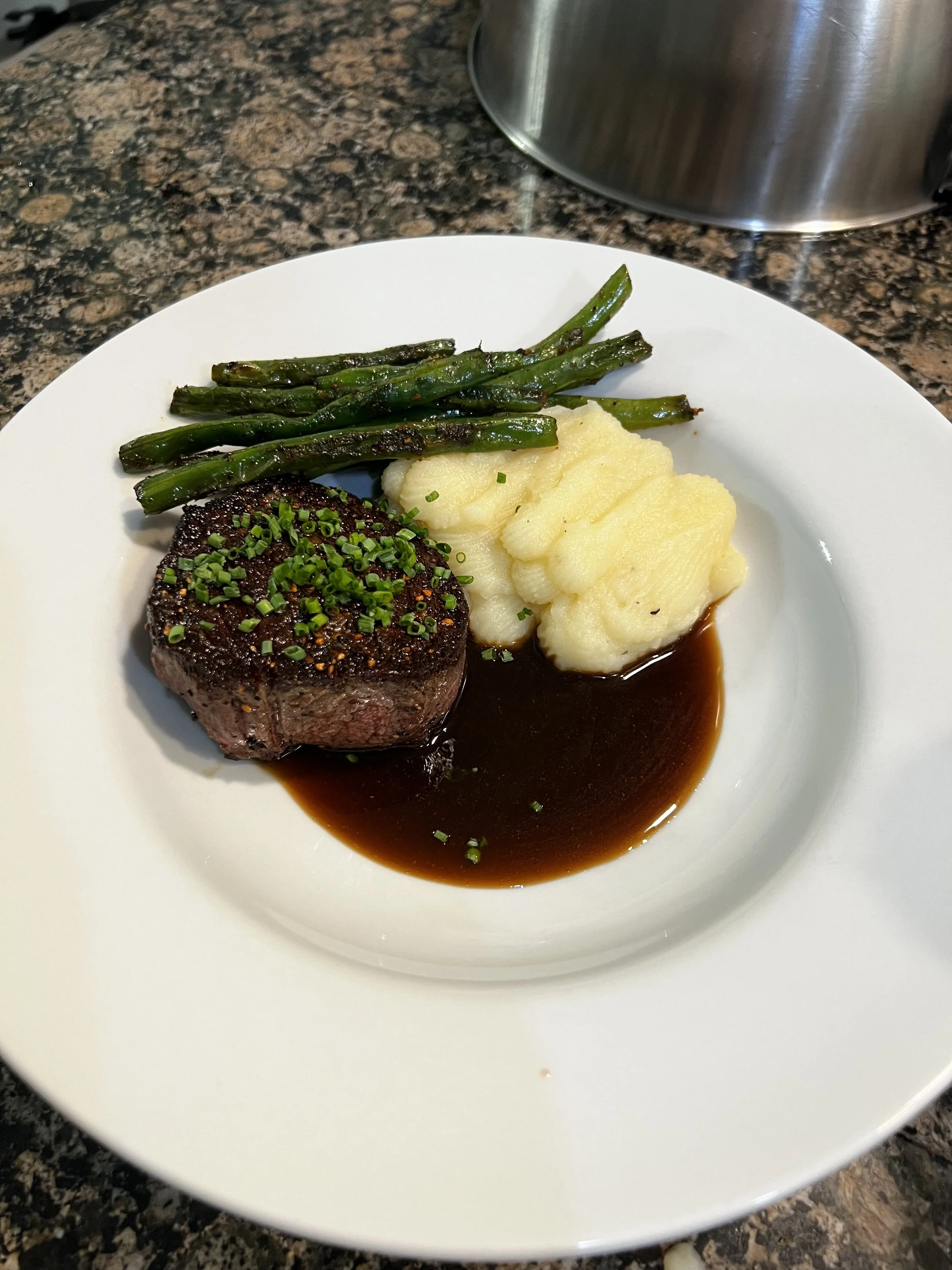 A plate with beef tenderloin, mashed potatoes, and green beans on a granite countertop