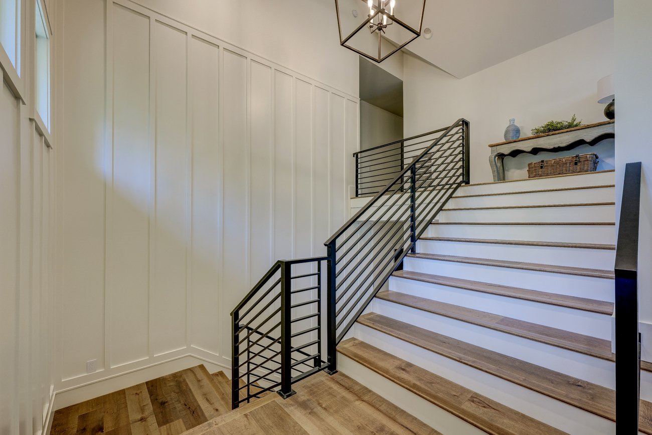 Modern staircase with black metal railing, wood steps, white walls, wooden floor, and a decorative console table with basket and vase on top.