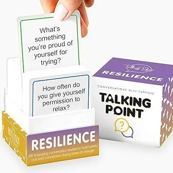 Two stacks of question cards, one purple and one white, along with a purple box labeled 'RESILIENCE' and a white box labeled 'TALKING POINT'. The purple box features the phrase 'Conversations with purpose'.