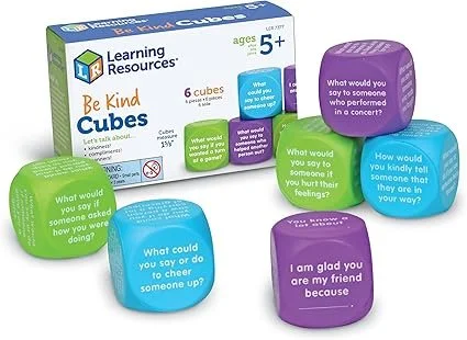Set of six colorful cubes with questions and statements for children, placed around a box of Be Kind Cubes learning resource. The cubes are green, blue, and purple, each with different prompts about kindness and social skills.