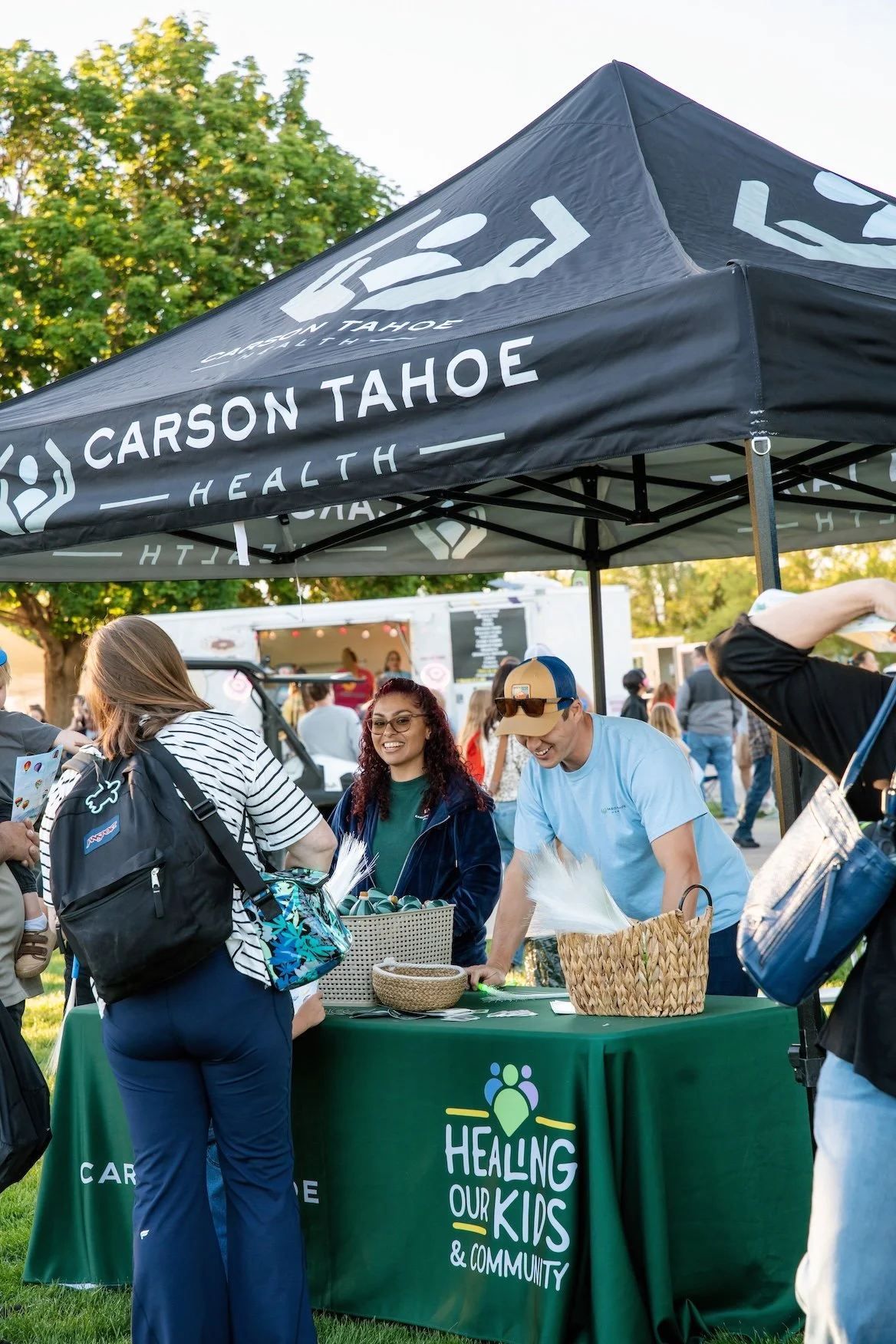 People gathered at an outdoor event under a Carson Tahoe Health tent, with a table displaying informational materials and a banner promoting healing for kids and community.