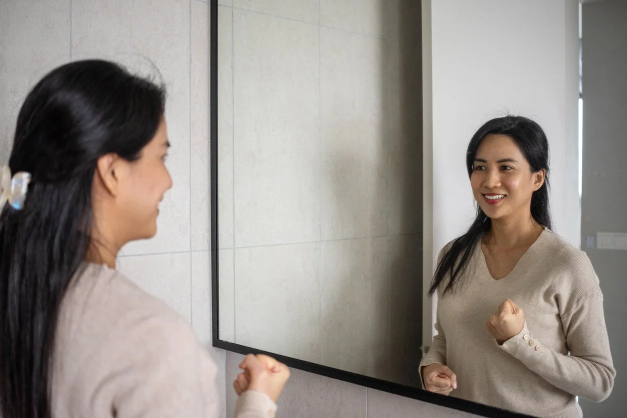 A woman smiles at her reflection with fists raised, practising a mirror boundary-setting exercise.