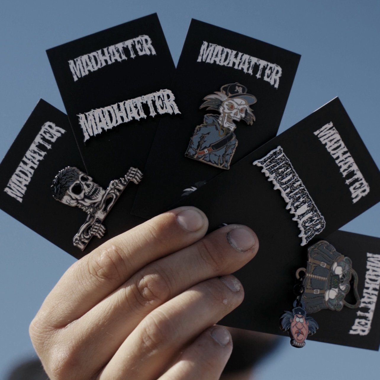 Hand holding five black cards with punk and metal band themed stickers, including skulls, skeletons, and band logos.