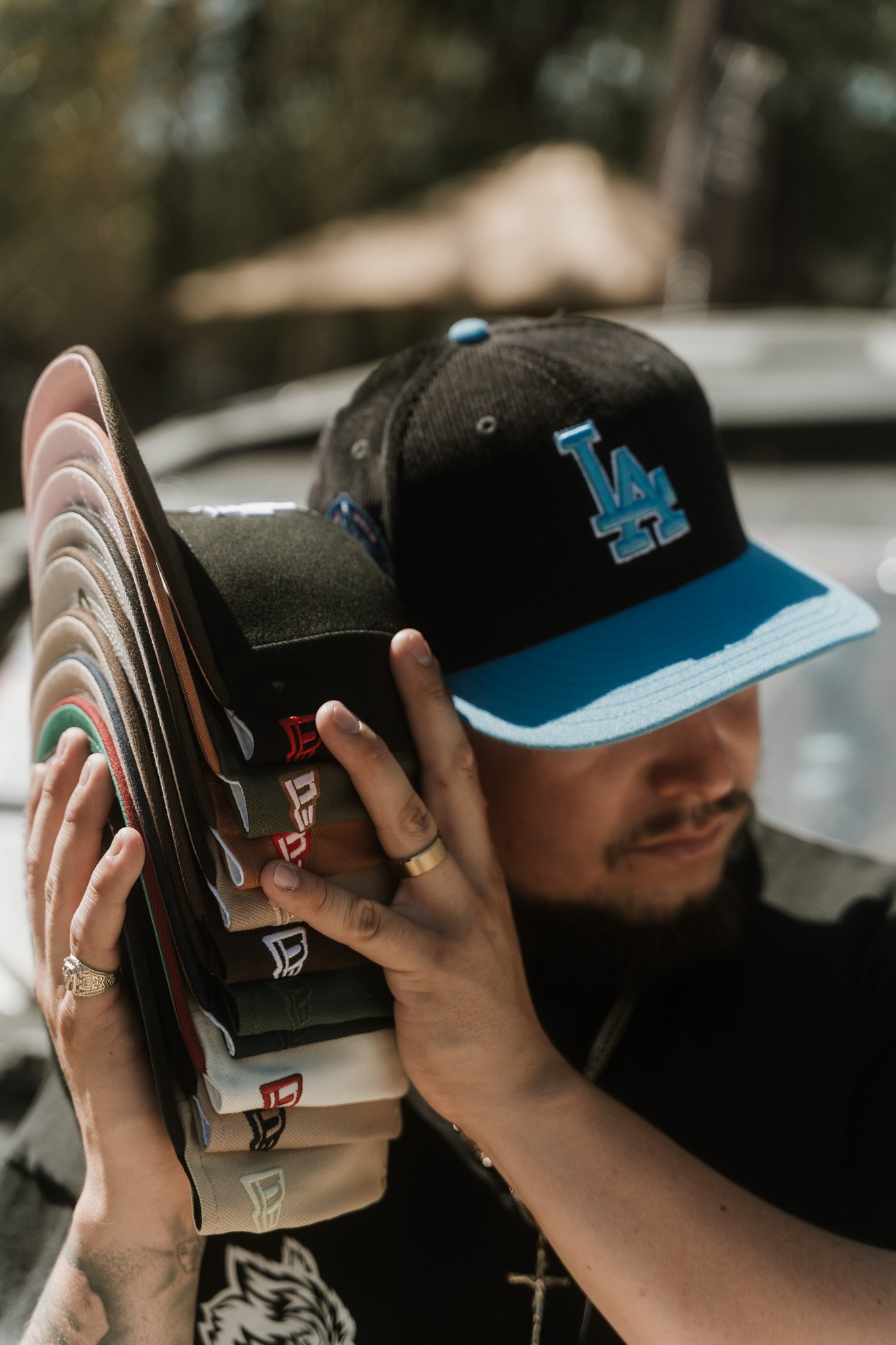 Person wearing a black Los Angeles Dodgers cap, holding a stack of belts, outdoors.