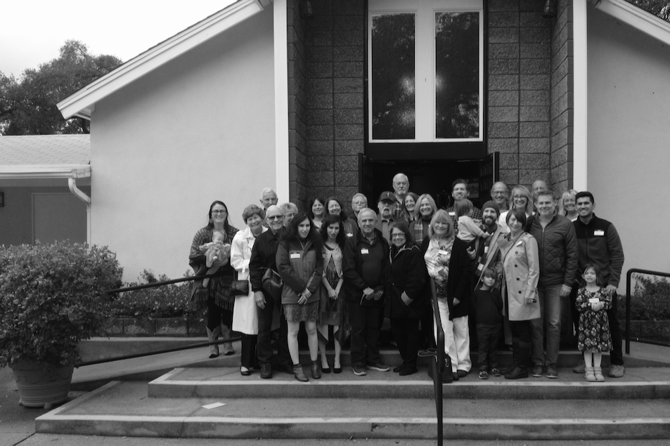 A group of people gathered outside a local church building for a photo in black and white.