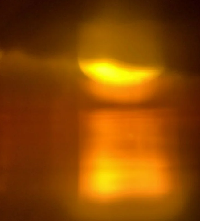 Blurry image of a bright yellow-orange light reflected on a dark surface.